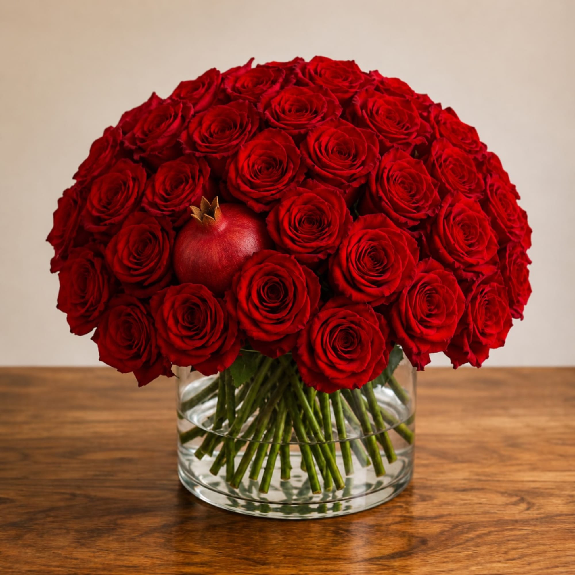Red rose bouquet in a clear glass vase with a pomegranate accent