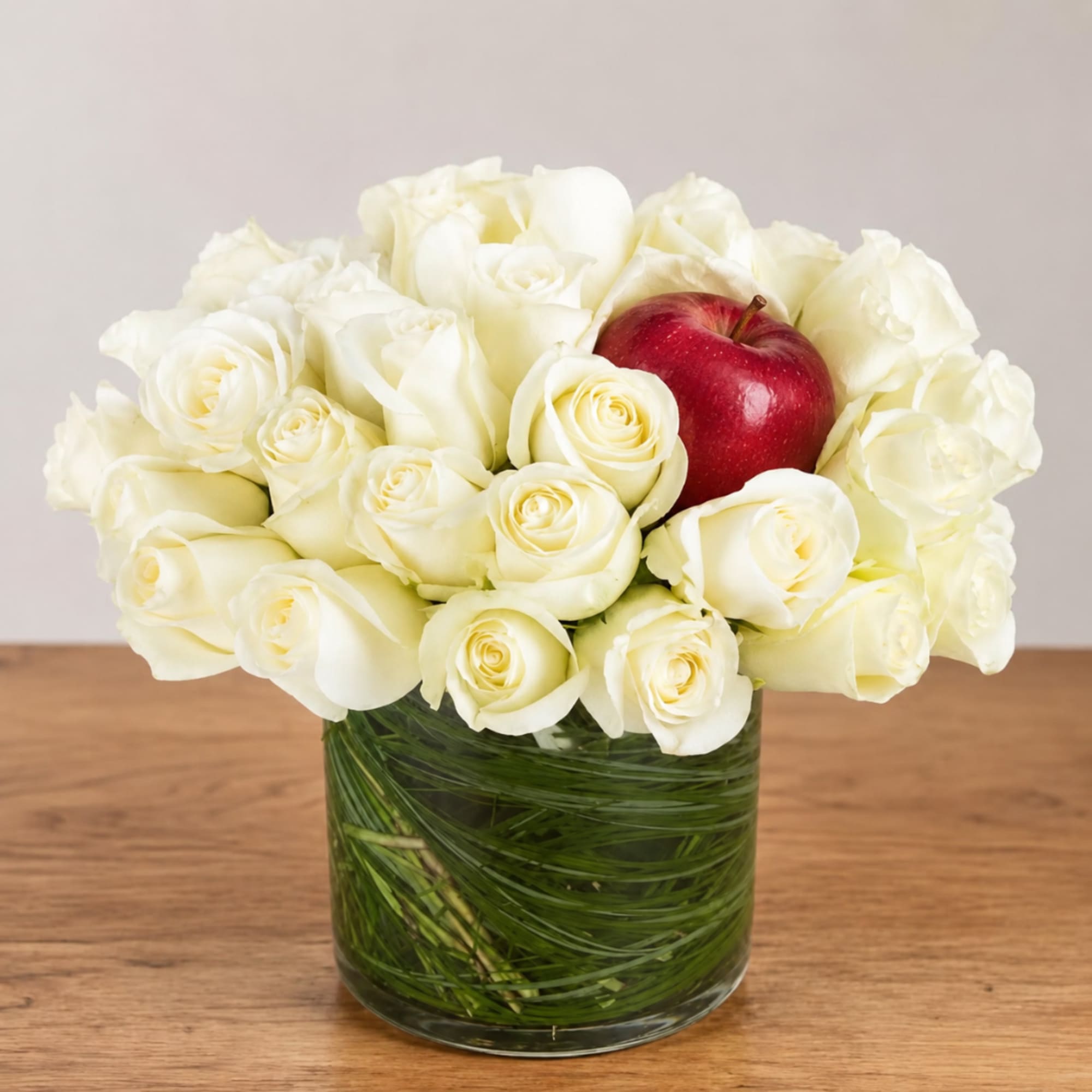 White roses in a glass vase with a red apple centerpiece
