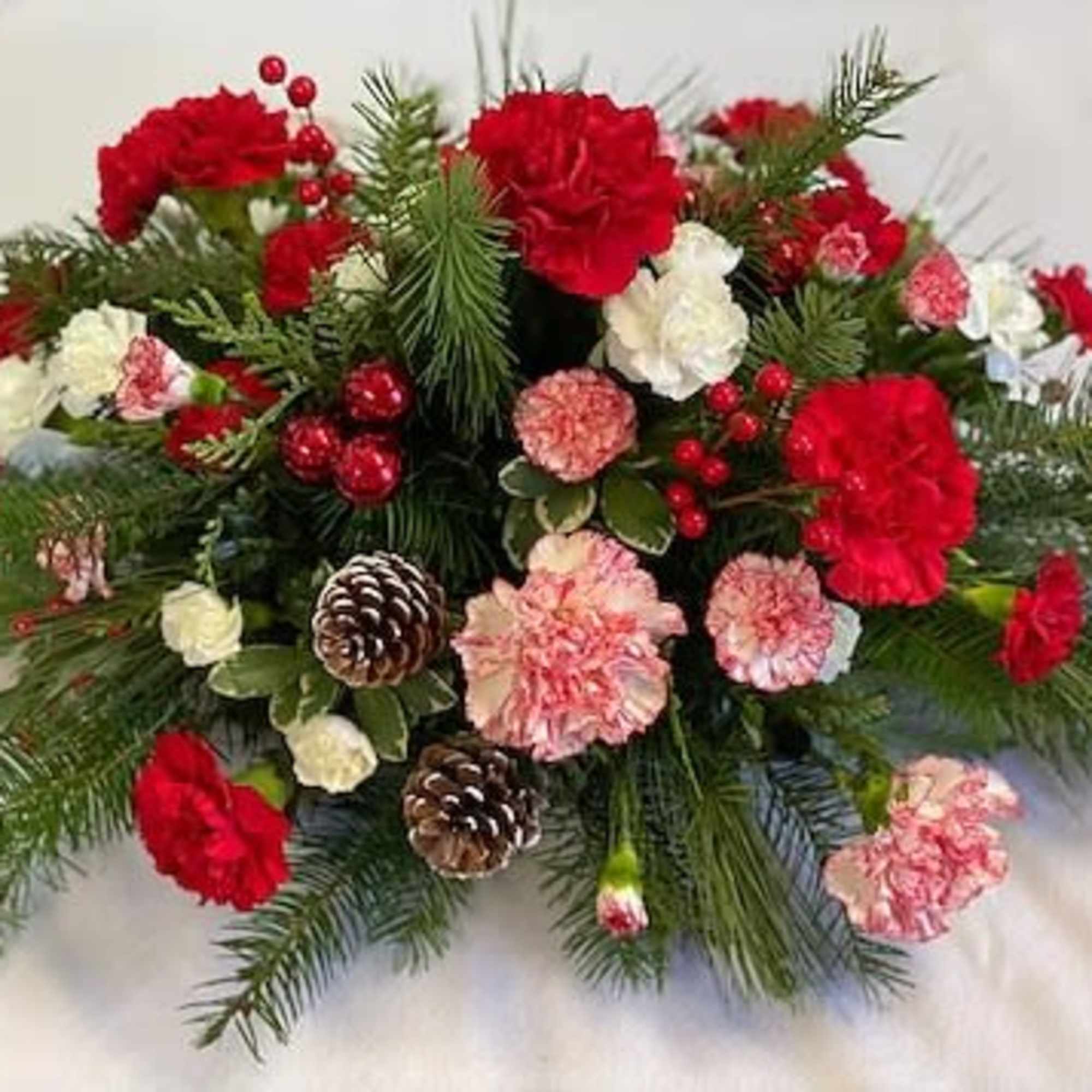 Red and pink carnations with pinecones in a holiday arrangement