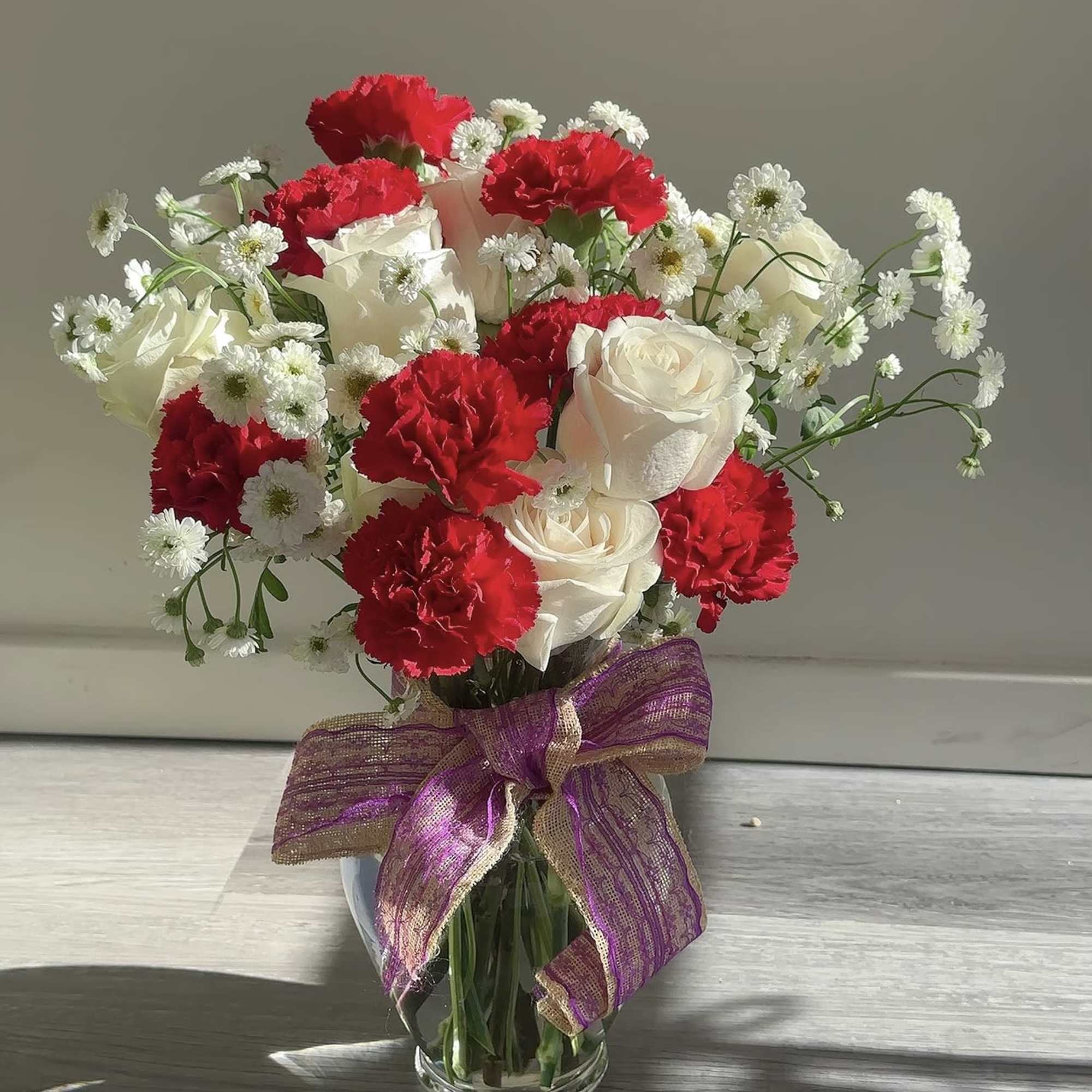 Bouquet of red carnations and white roses in a glass vase with a purple ribbon