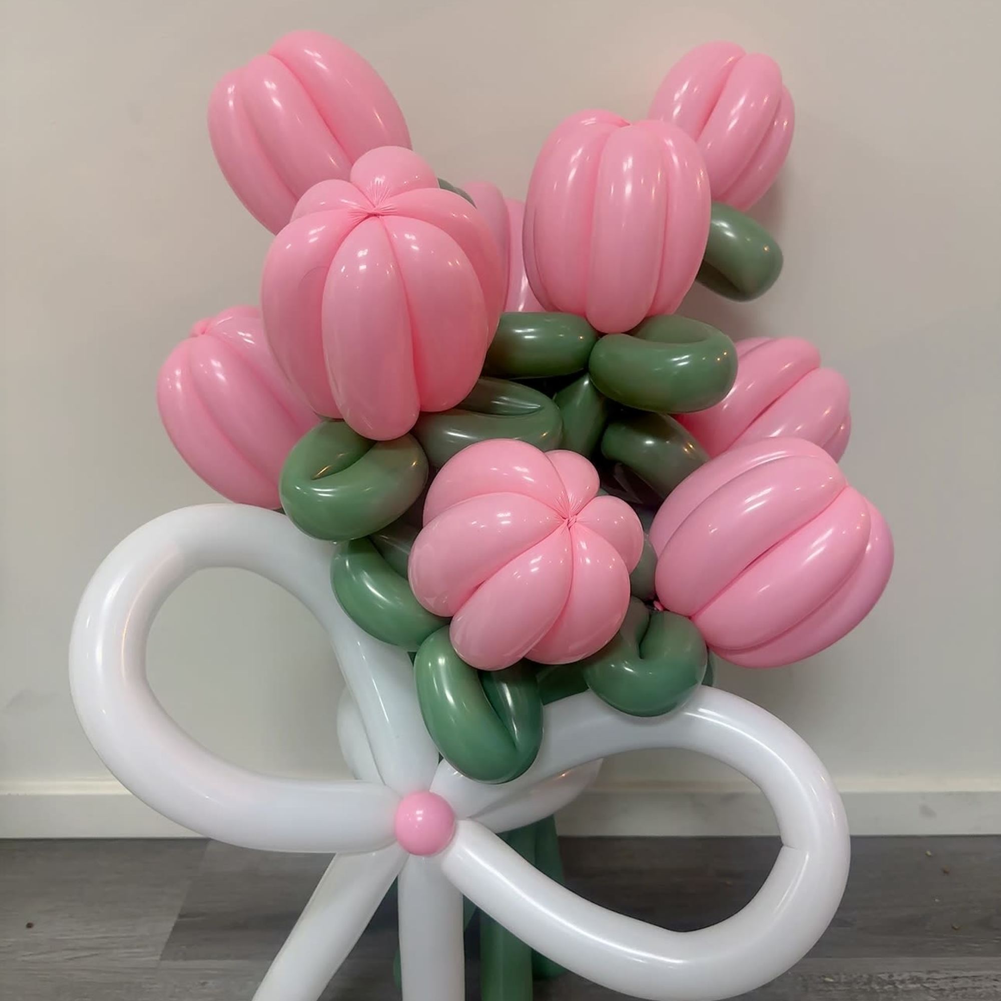 Pink and green balloon bouquet shaped like flowers with a white bow