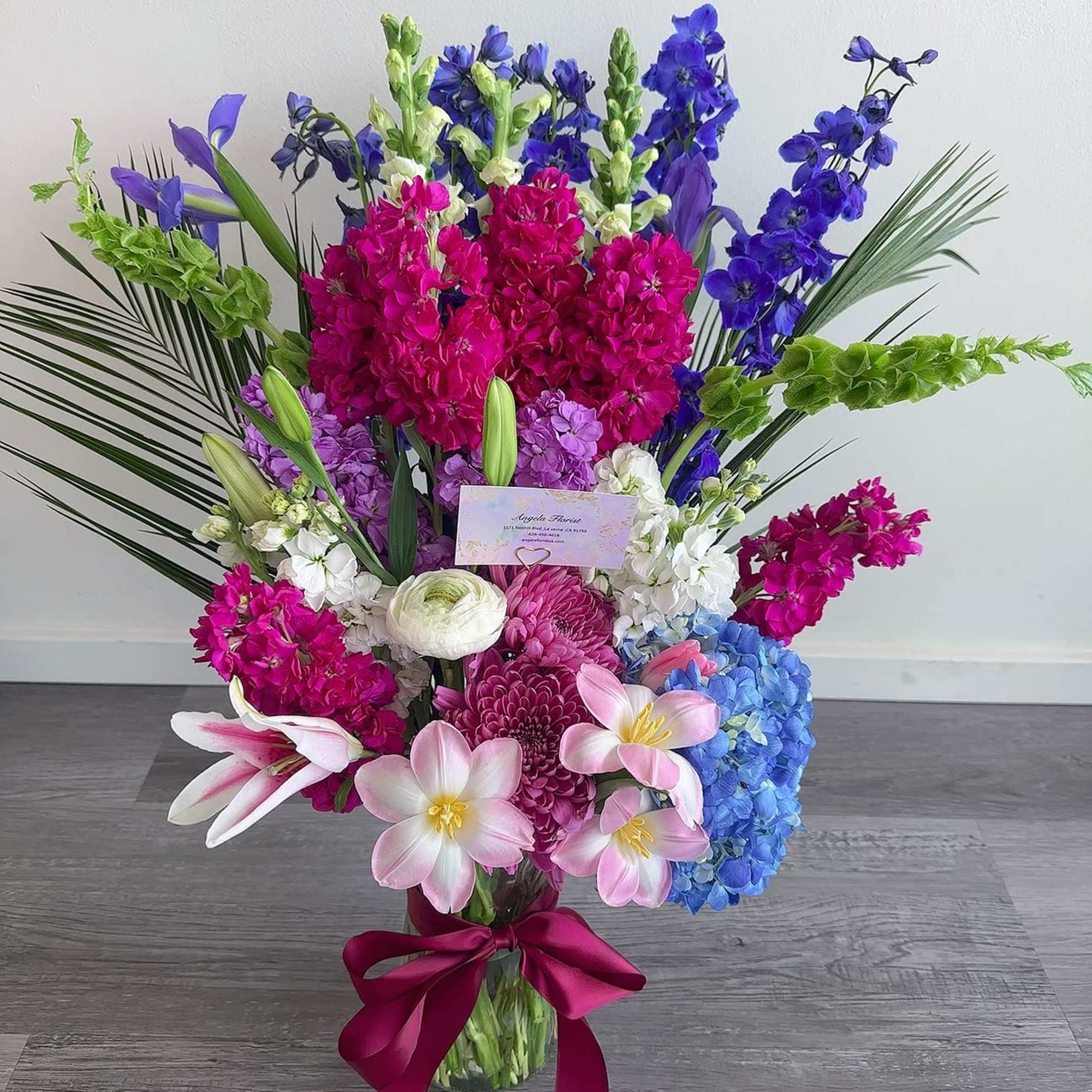 Tall bouquet of pink, blue, purple, and white flowers in a glass vase
