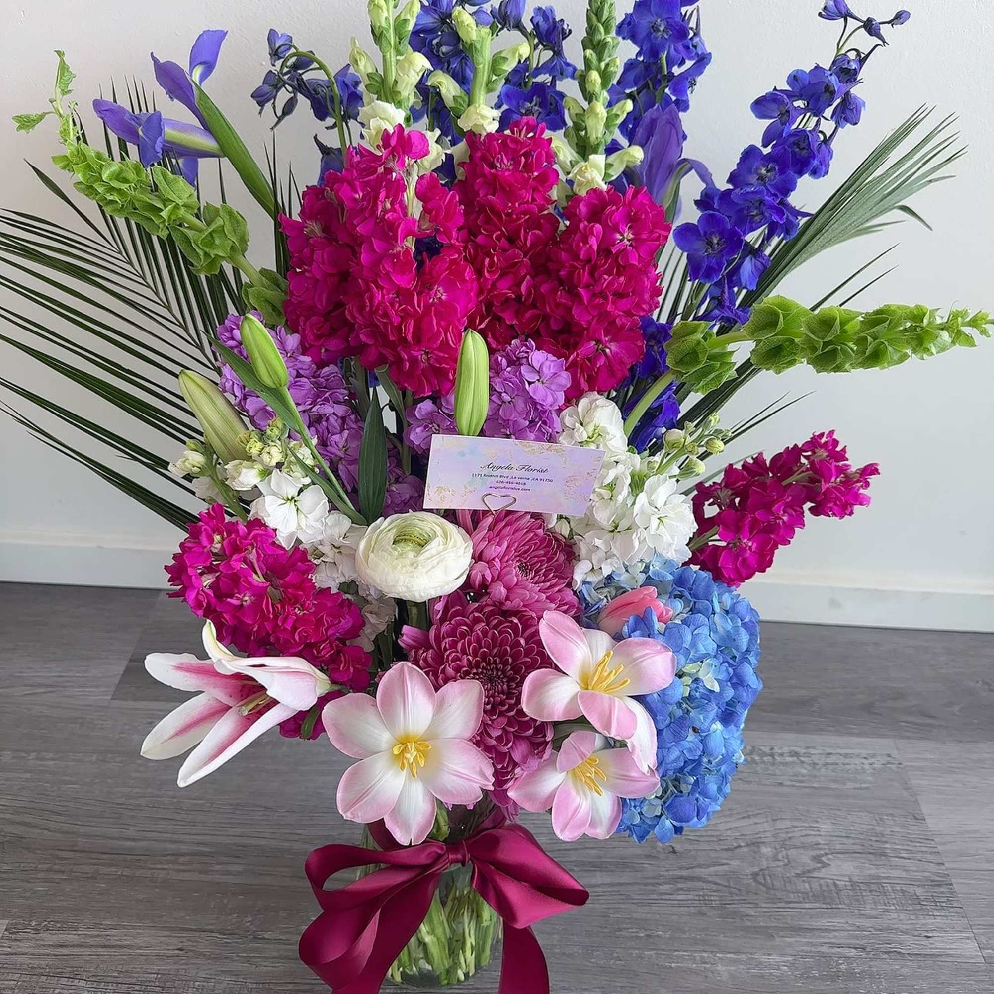 Tall bouquet of pink, purple, blue, and white flowers tied with a magenta ribbon