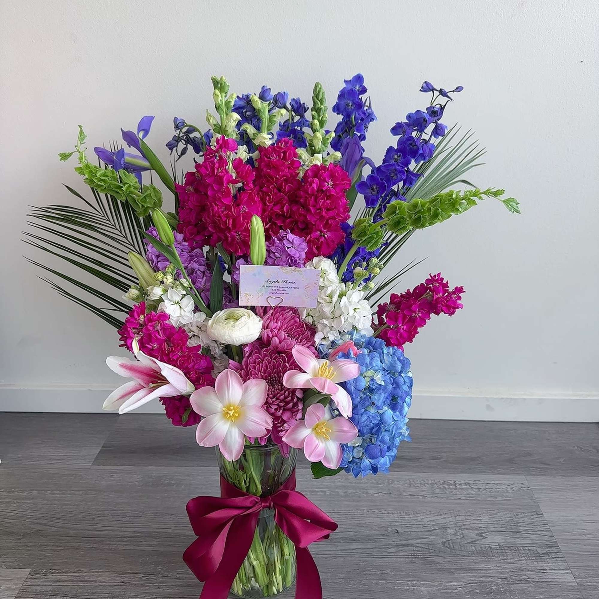 Tall mixed bouquet in a glass vase with pink, blue, and purple flowers