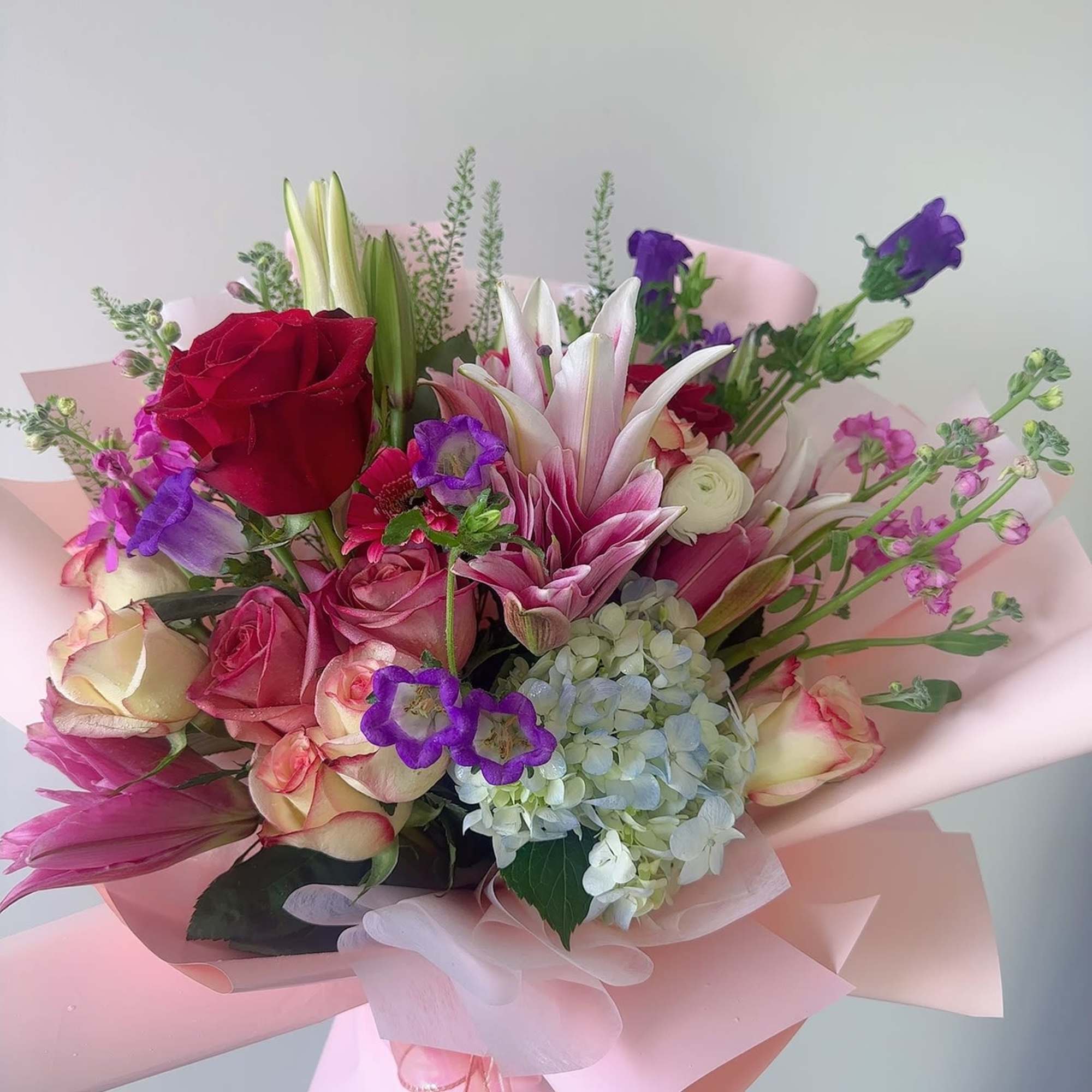Bouquet of pink and red roses with lilies and purple blooms in pink wrap
