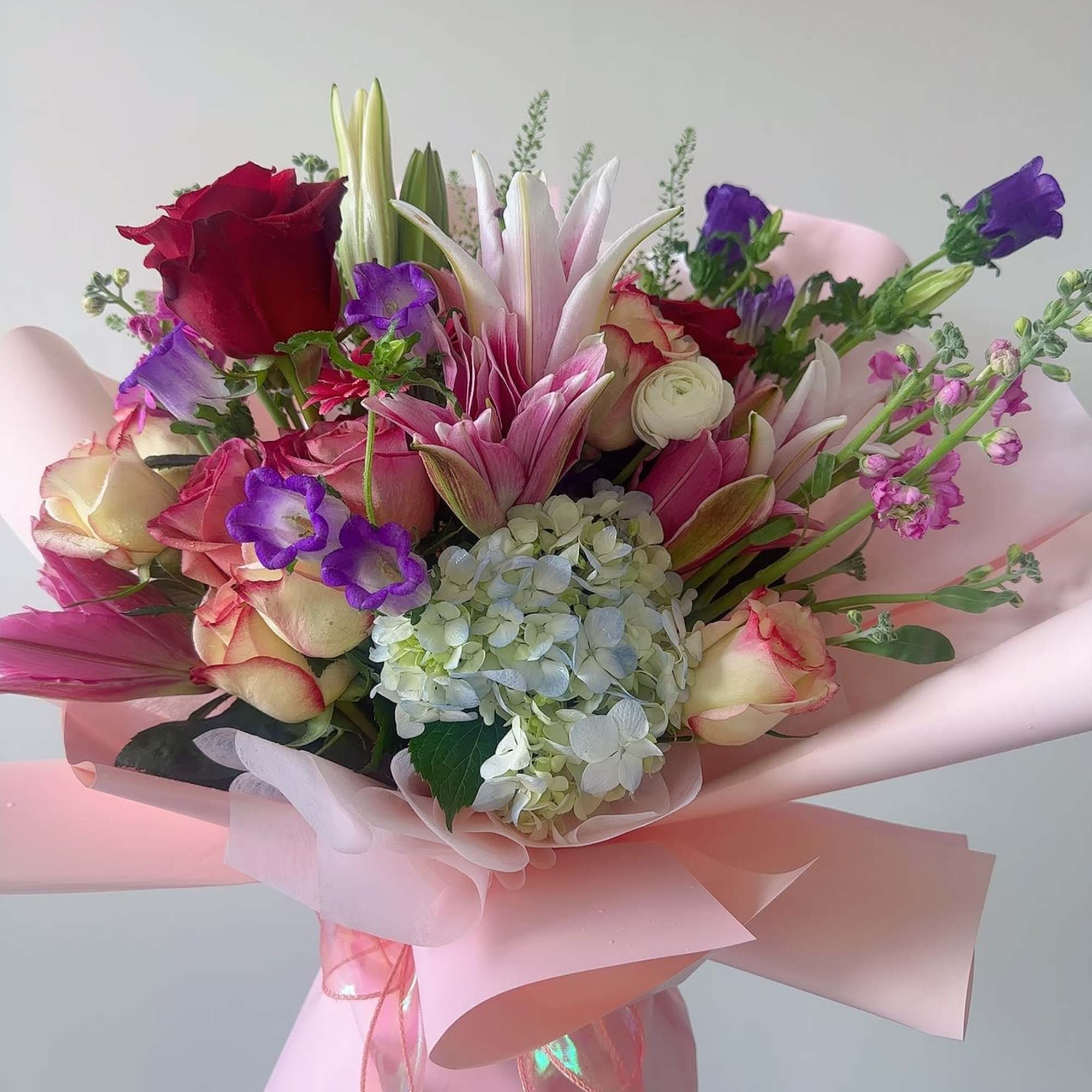 Pink and purple mixed bouquet with roses, lilies, and hydrangea wrapped in pink paper
