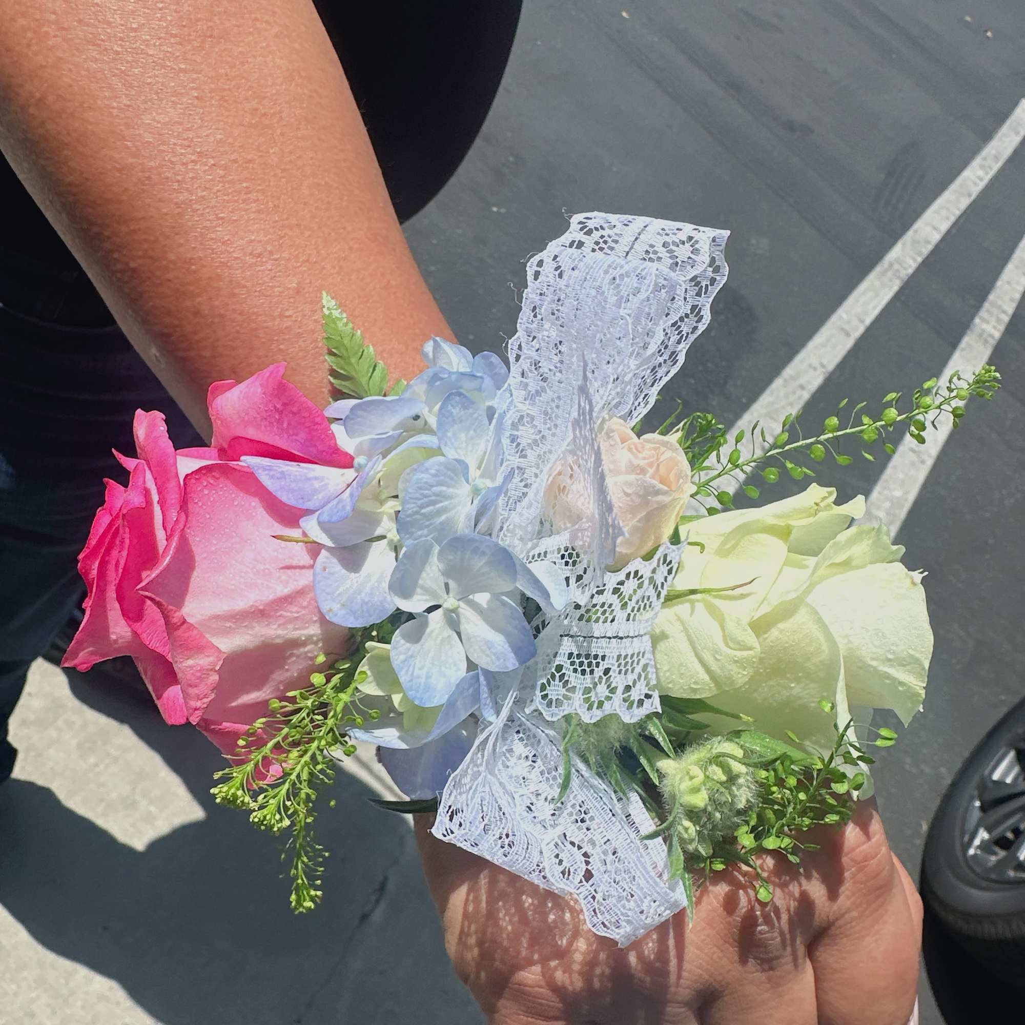 Small wrist corsage with pink and white roses and blue flowers tied with lace ribbon