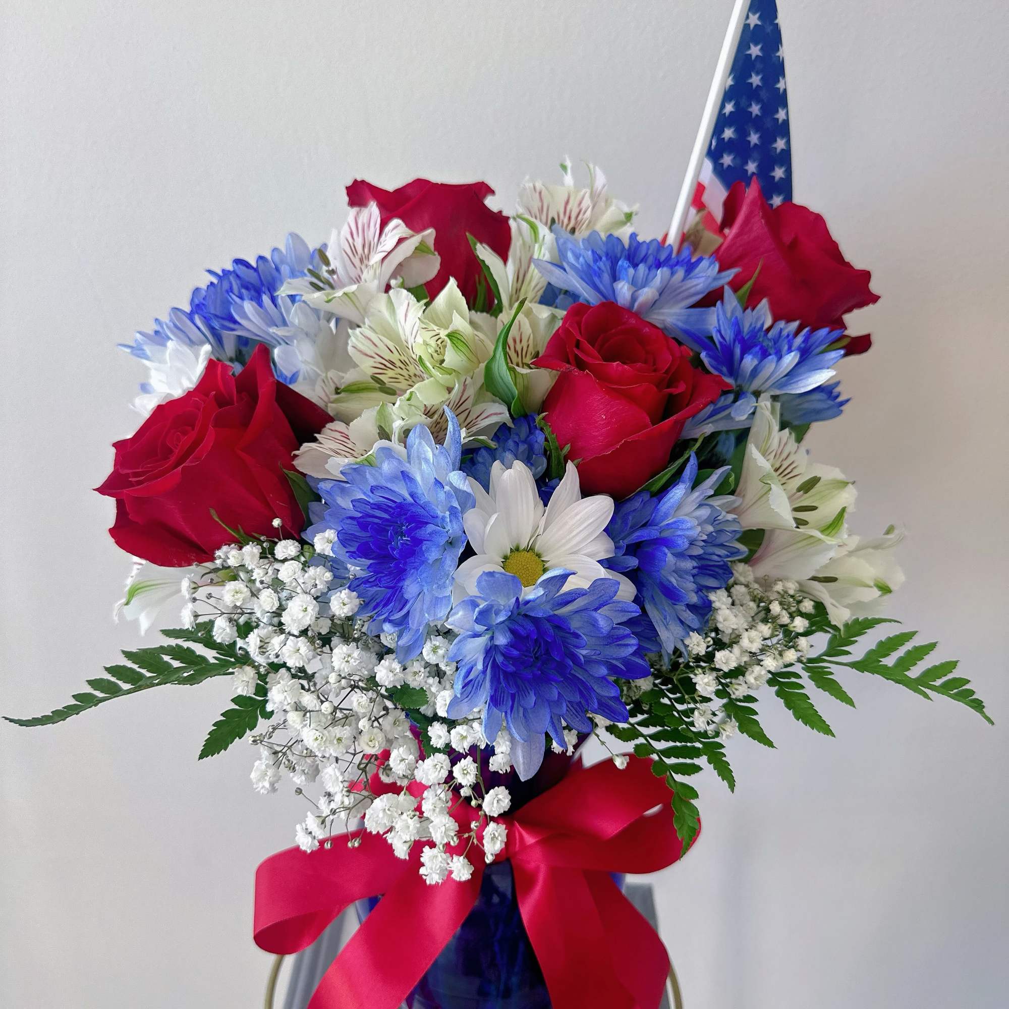 Bouquet of red roses, blue and white daisies, and baby's breath in a blue vase