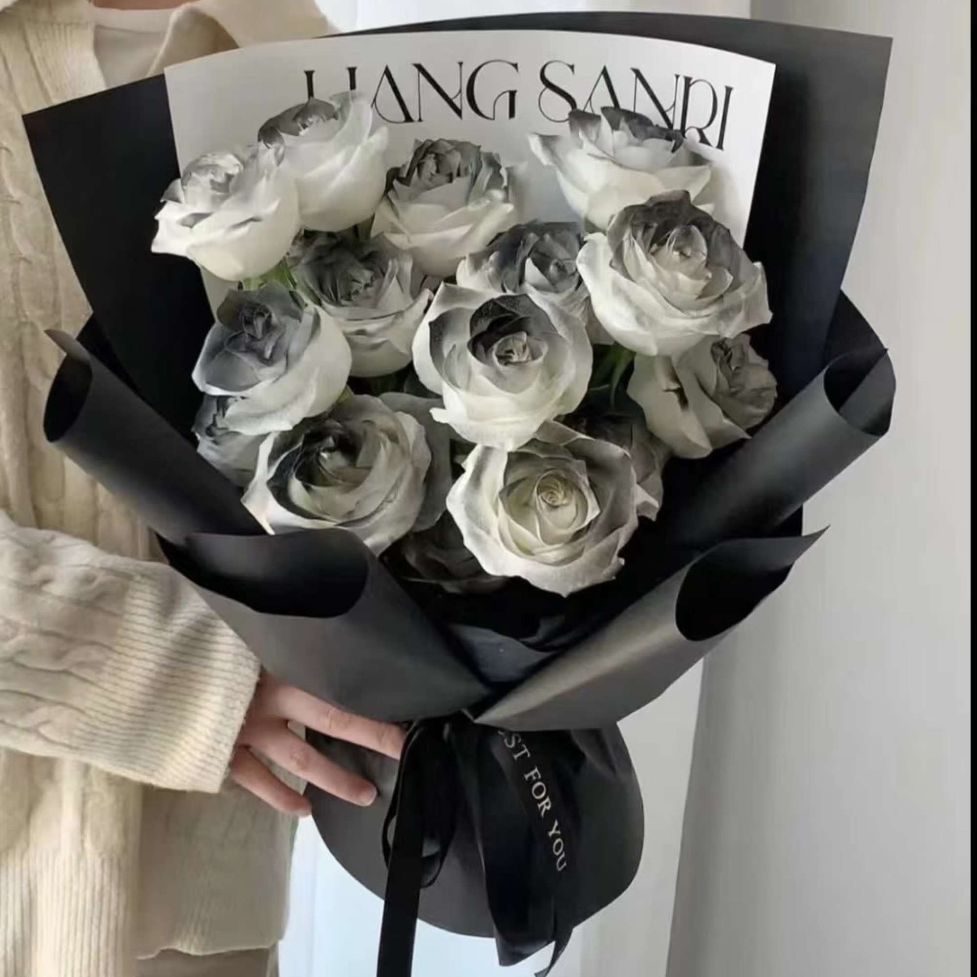 Bouquet of white roses with gray-tinted petals wrapped in black paper