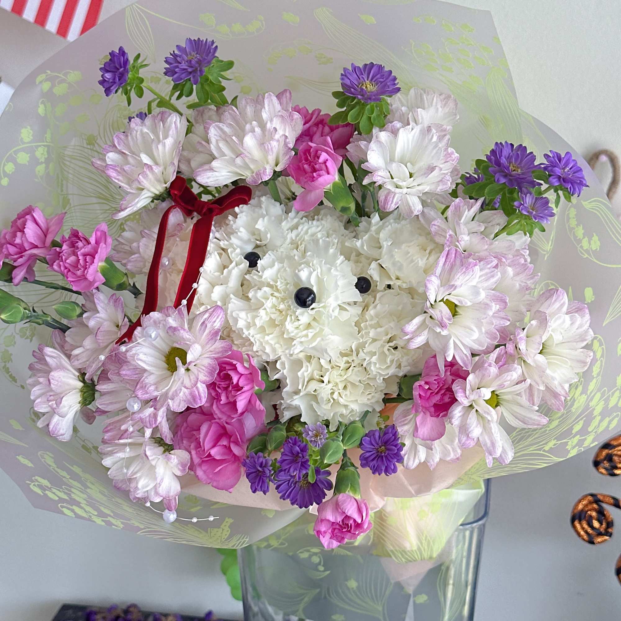 Bouquet of white, pink, and purple flowers in clear wrap with a red ribbon