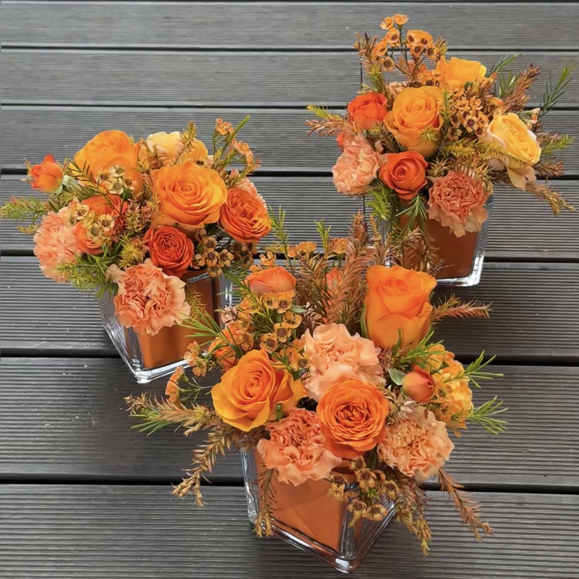 Three orange floral arrangements in square glass vases
