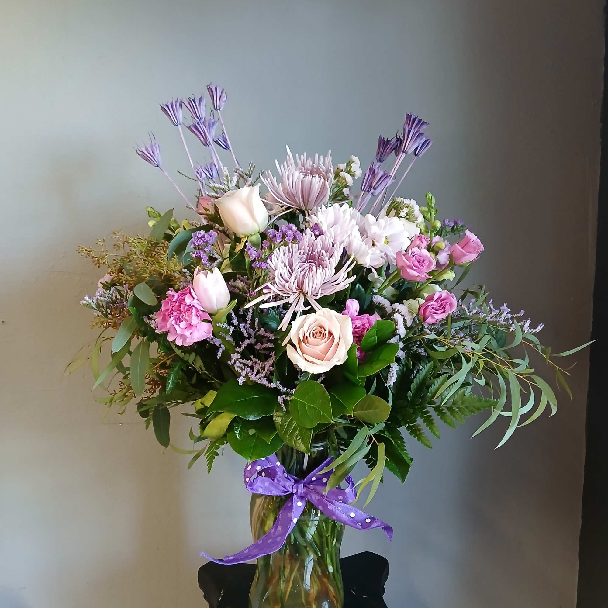 Mixed pink and lavender bouquet in a glass vase with a purple ribbon.