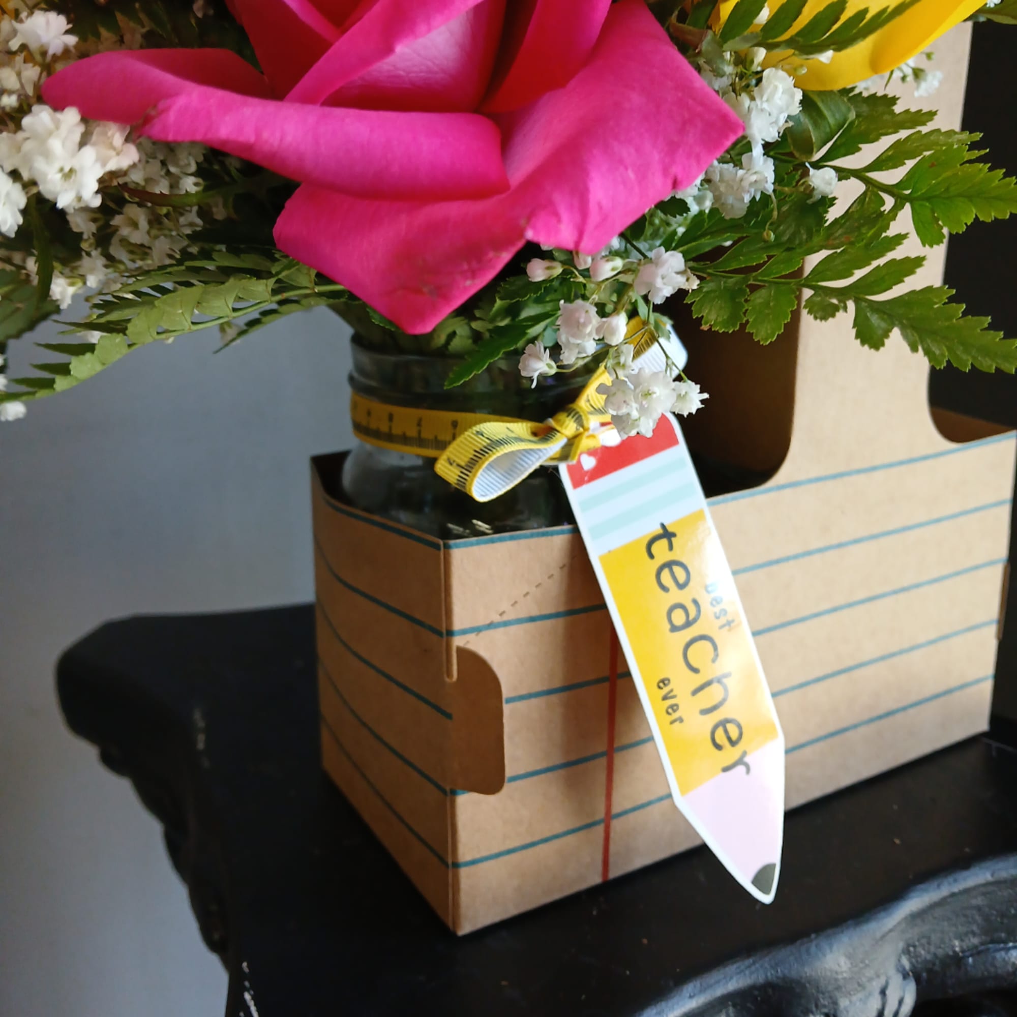 Pink and yellow flowers in a glass jar with a gift tag