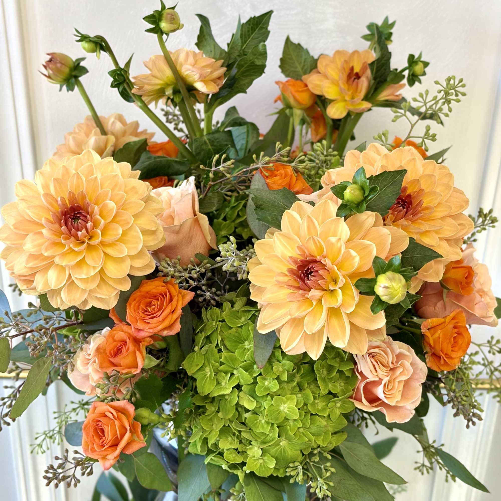 Orange dahlias and roses arranged in a vase with green hydrangea