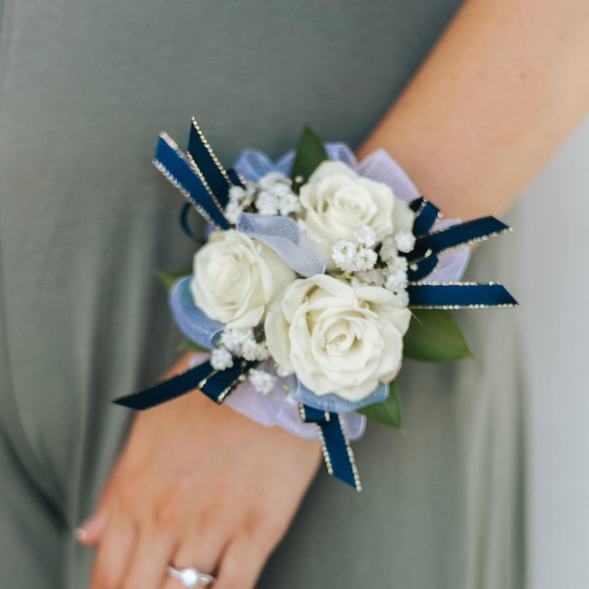 Wrist corsage of white roses with baby's breath and navy and sheer ribbons.