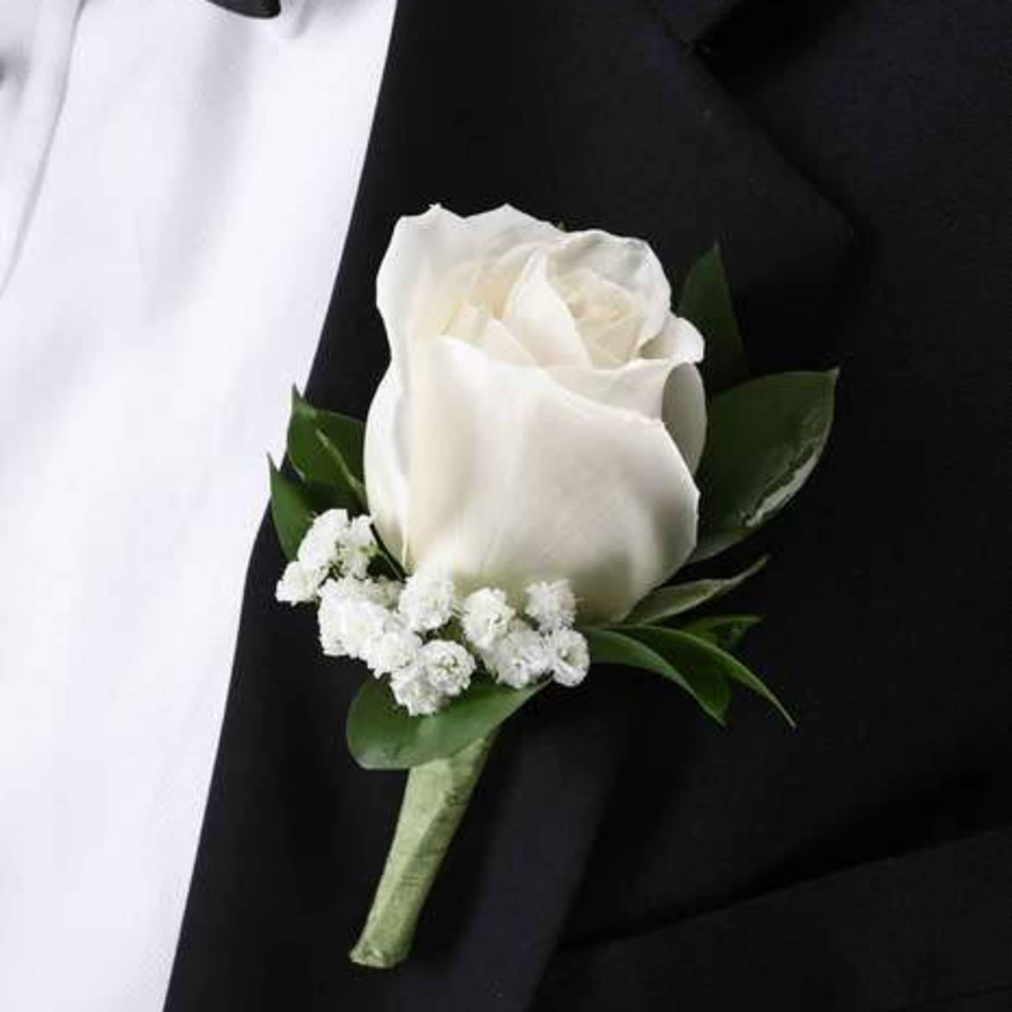 White rose boutonniere with small white filler flowers pinned to a black suit lapel