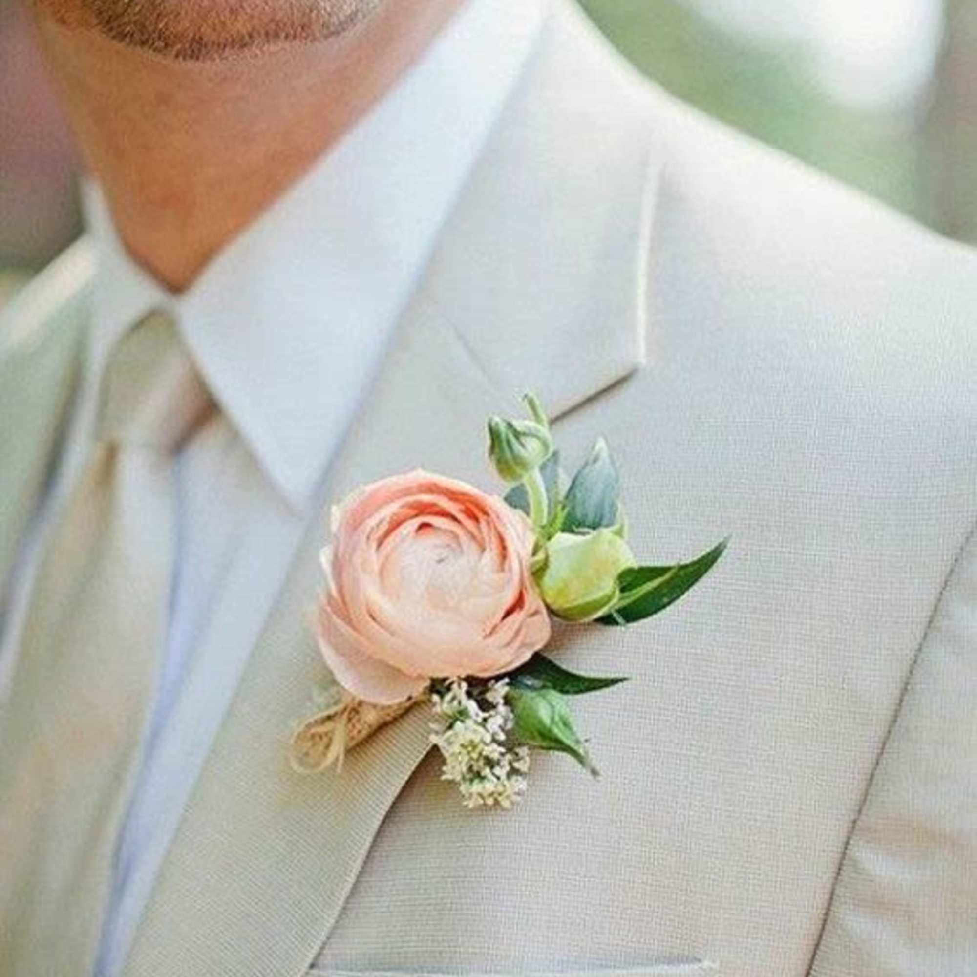 Boutonniere with a blush ranunculus on a beige suit lapel