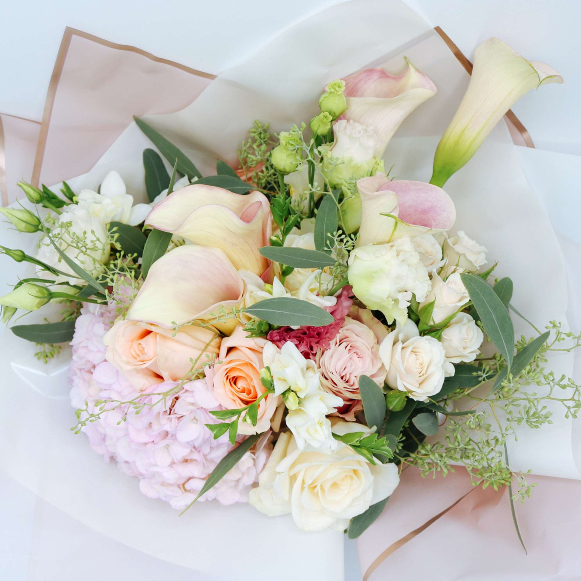 Pastel bouquet with calla lilies, roses, hydrangea, and freesia wrapped in white and blush paper