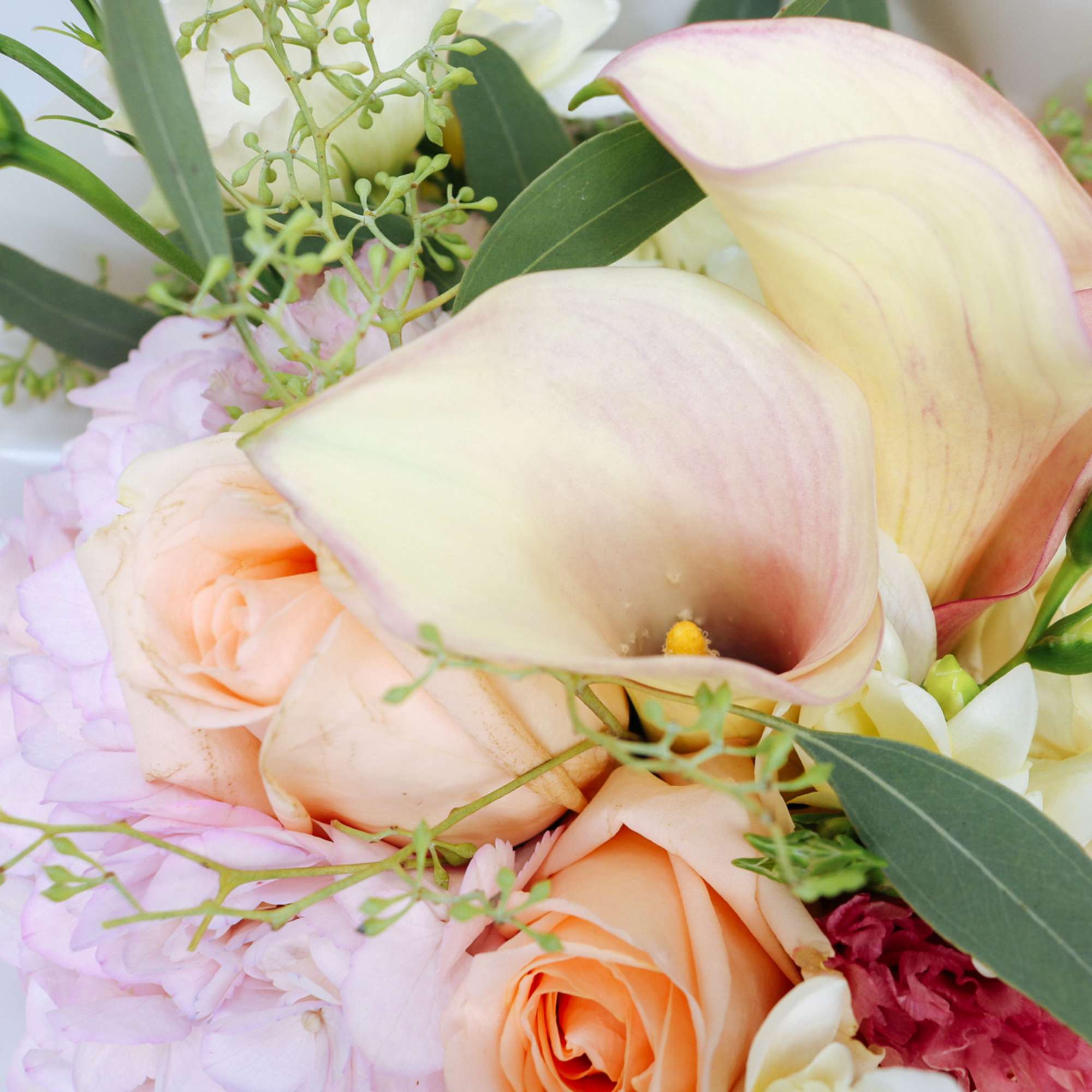 Close-up of pastel peach roses and cream calla lilies in a mixed bouquet