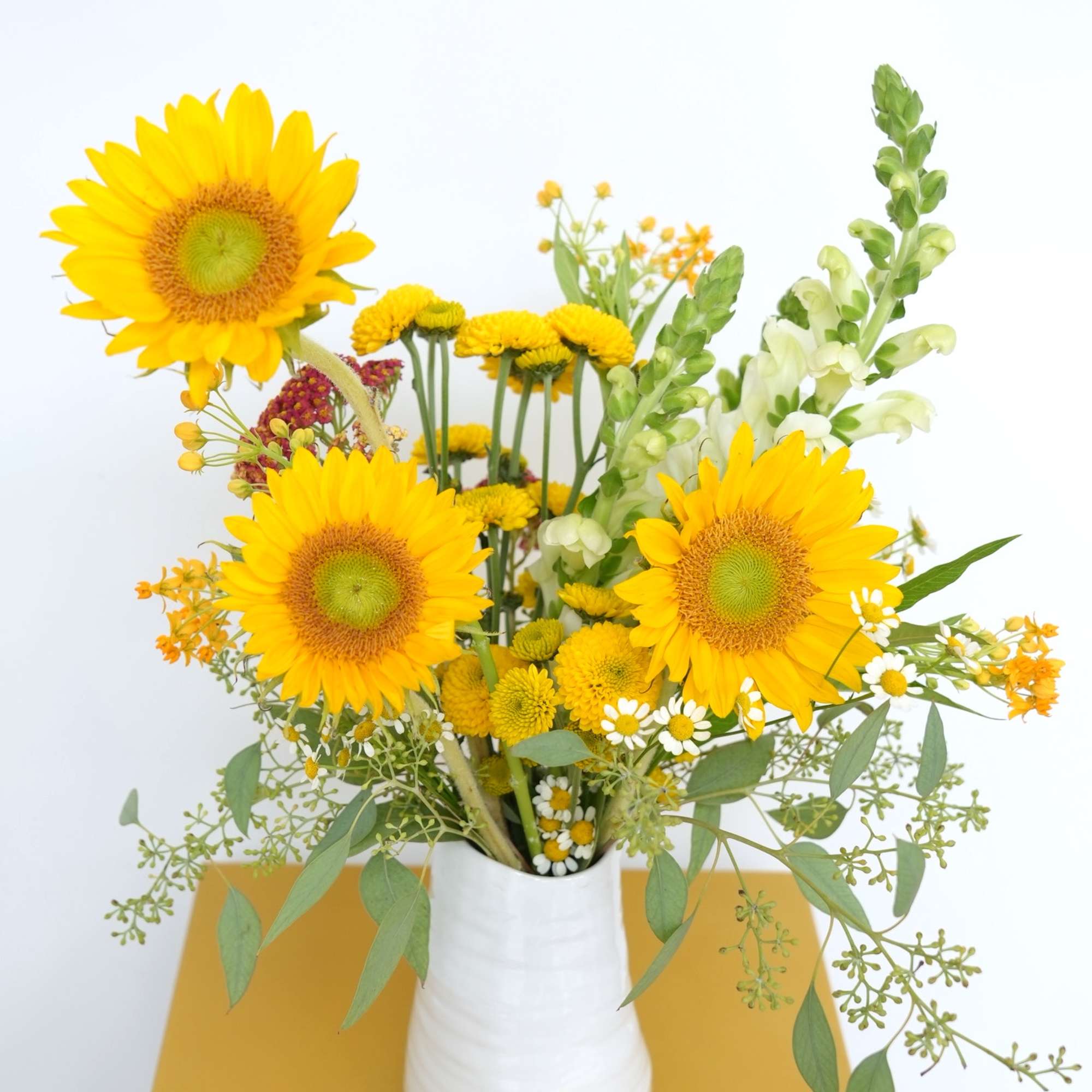 Yellow sunflower bouquet in a white vase with mixed small blooms