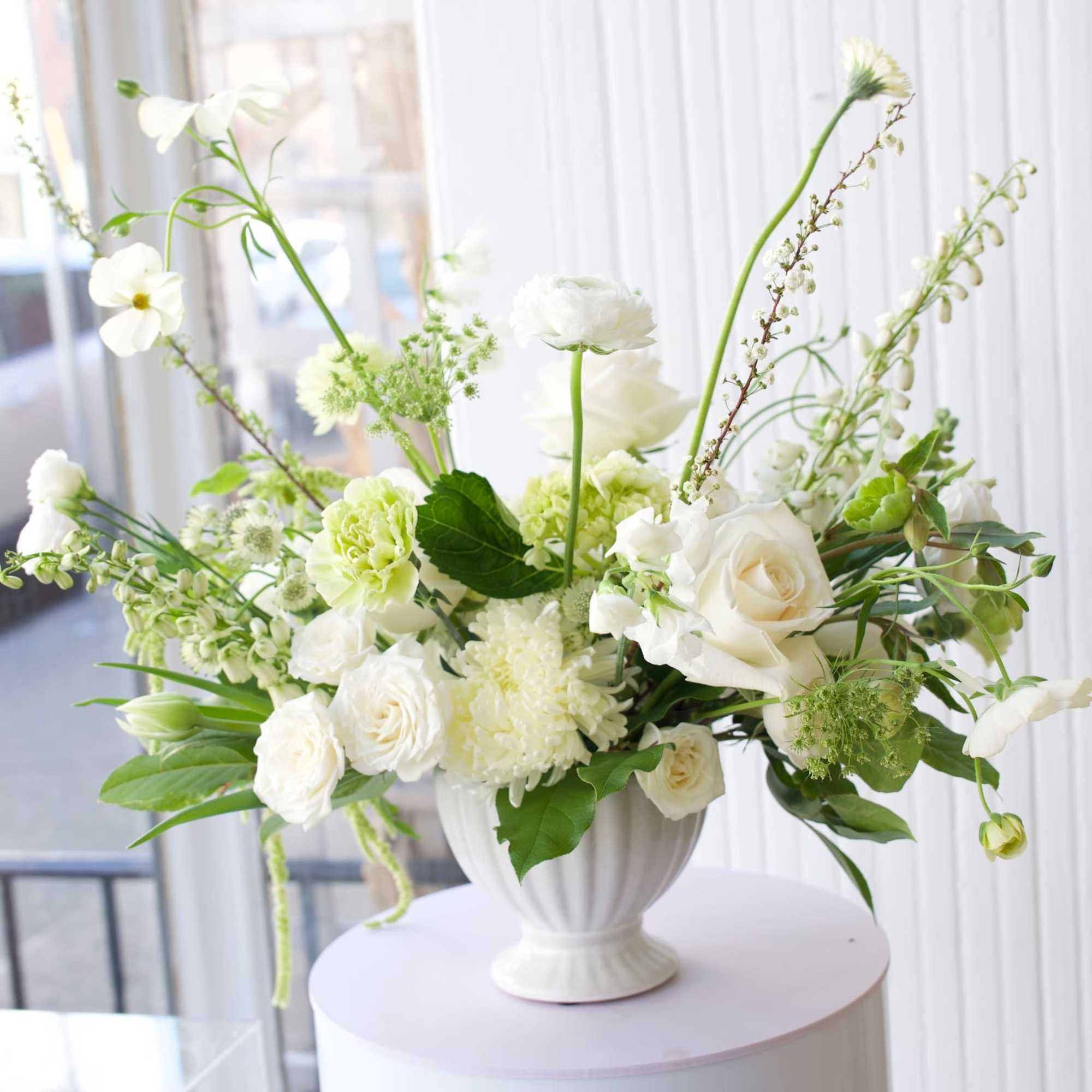 White floral arrangement in a white urn vase on a round pedestal