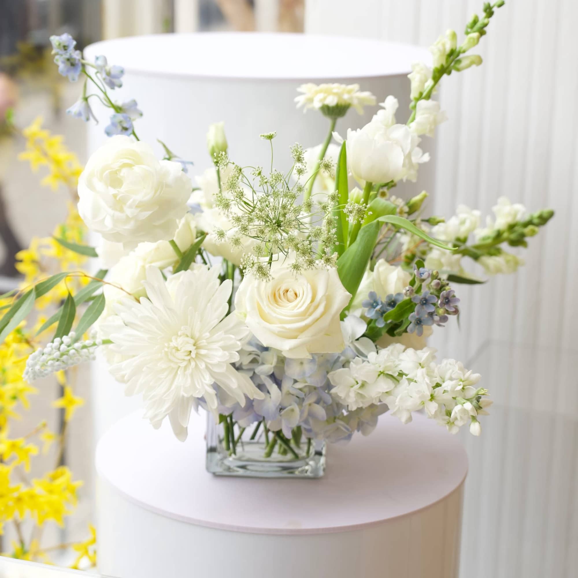 White floral arrangement in a clear square vase with blue accents