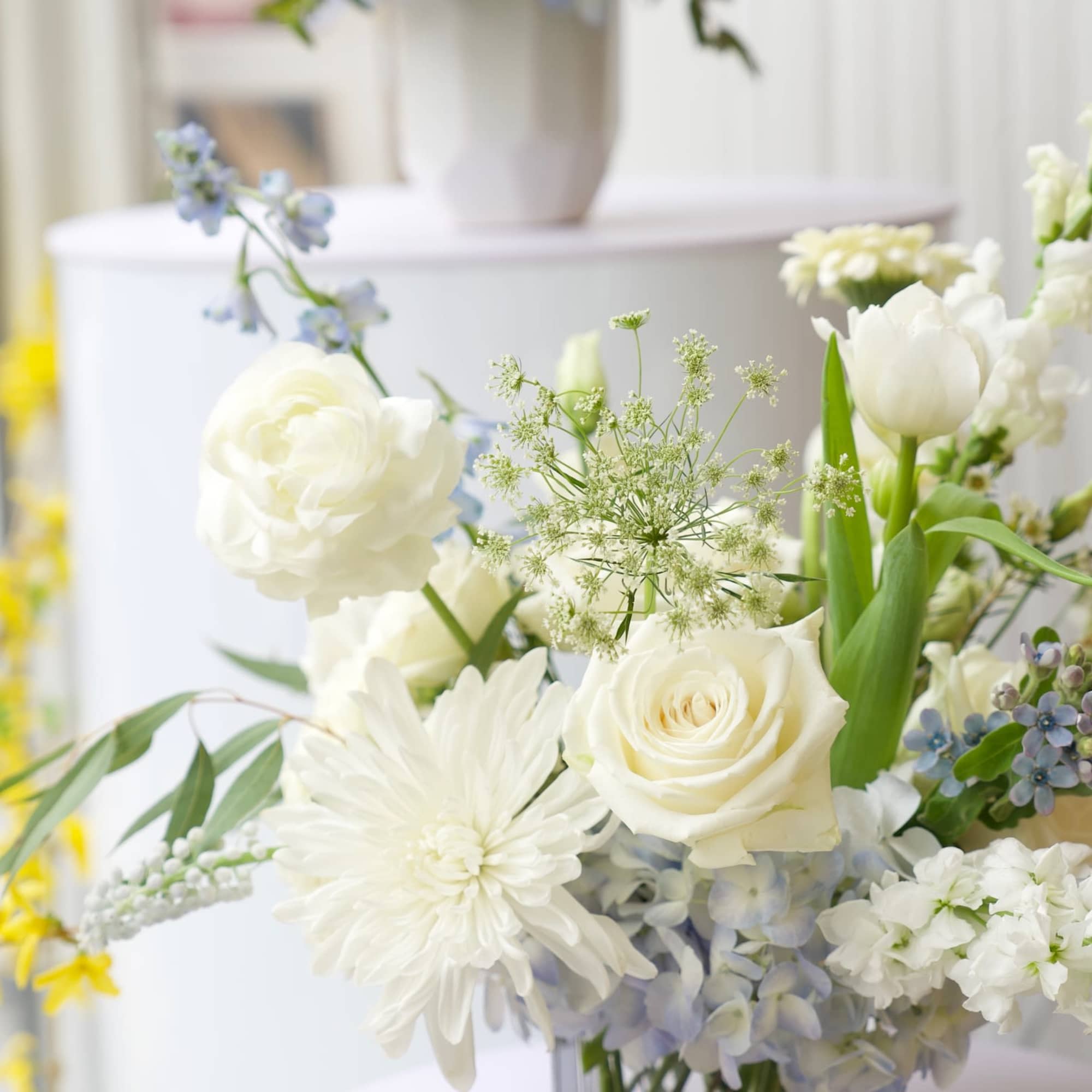 White floral arrangement in a square glass vase with roses and daisies