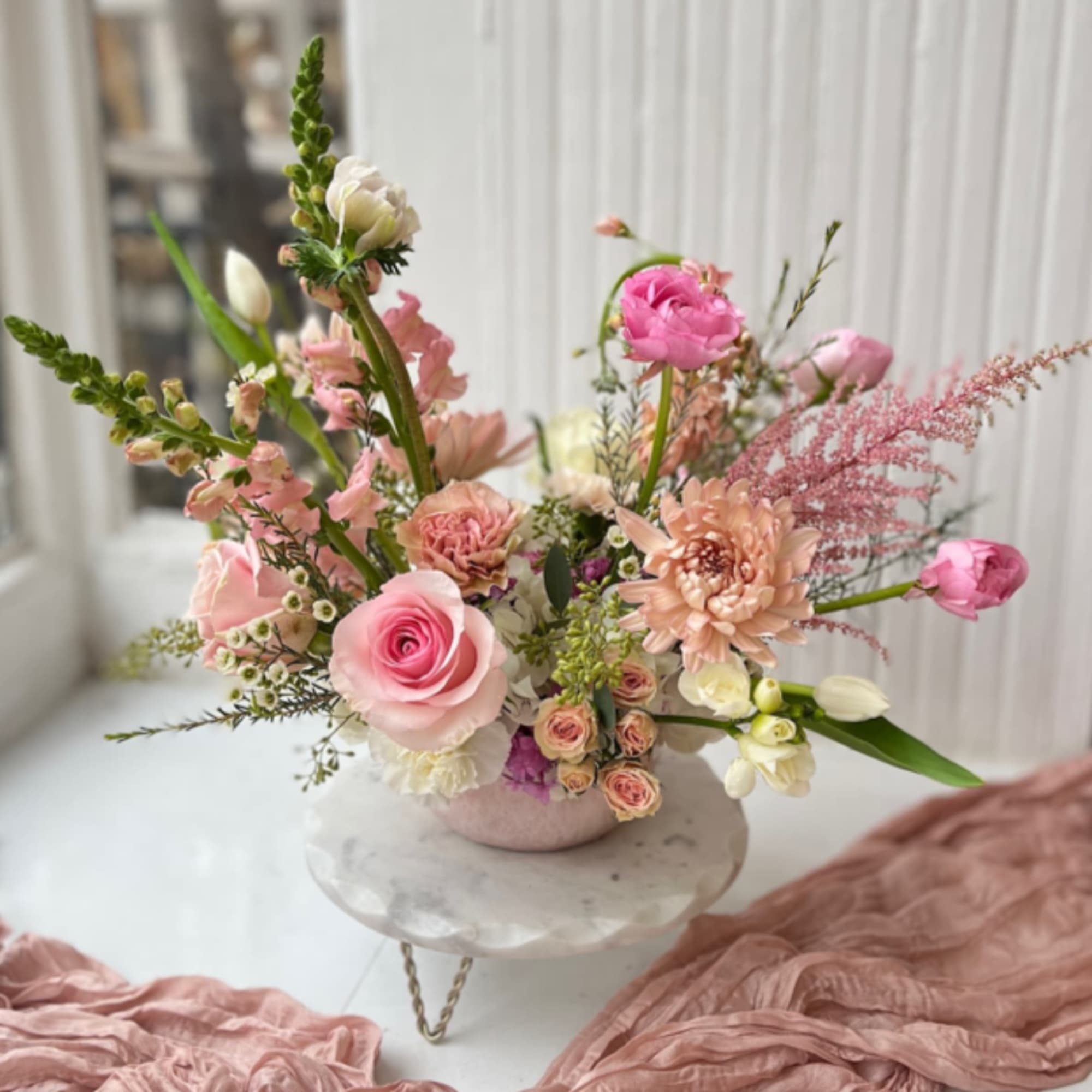 Pink and peach floral arrangement in a low vase on a pedestal