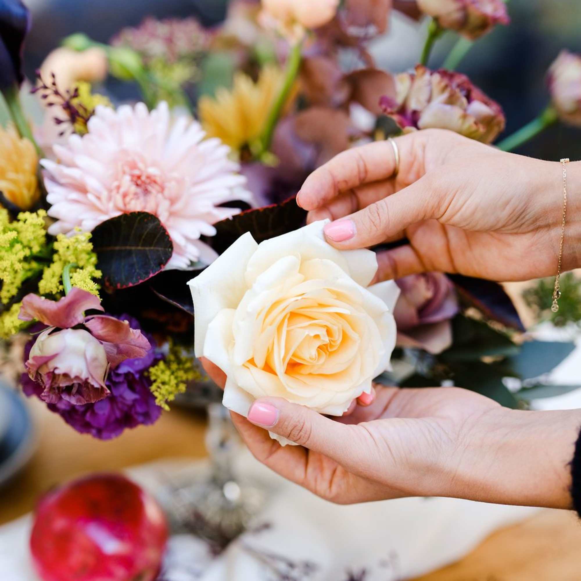 Hands holding a cream rose in front of a mixed floral arrangement