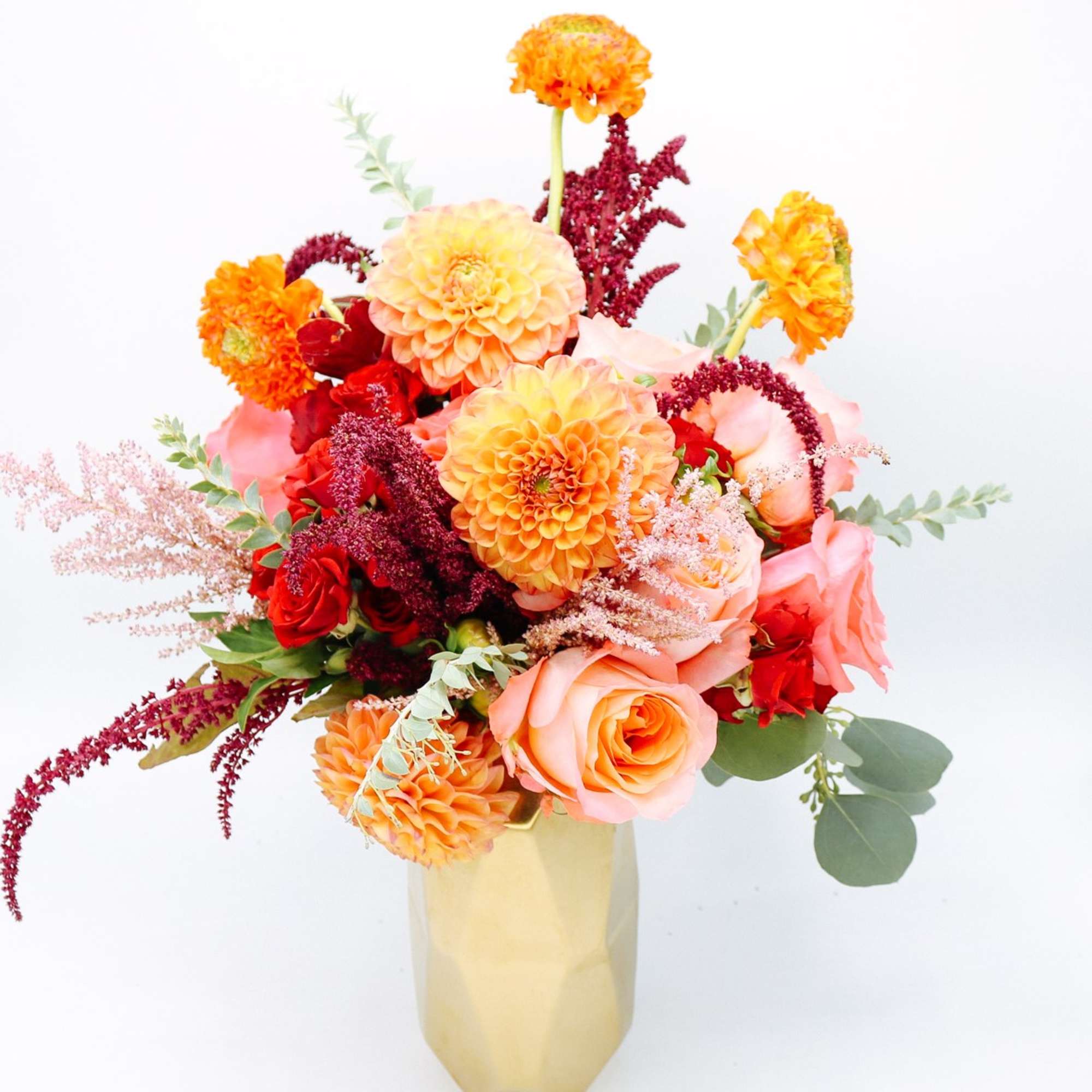 Bouquet of orange, pink, and red flowers in a gold vase