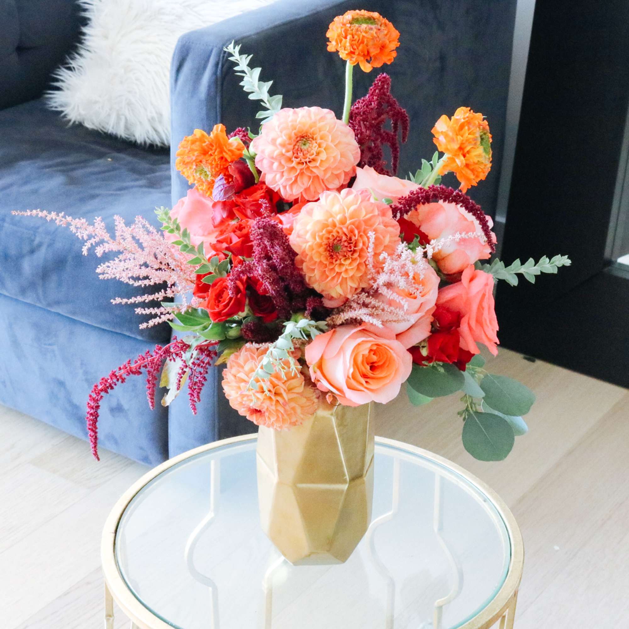 Bouquet of peach, orange, and red flowers in a gold vase