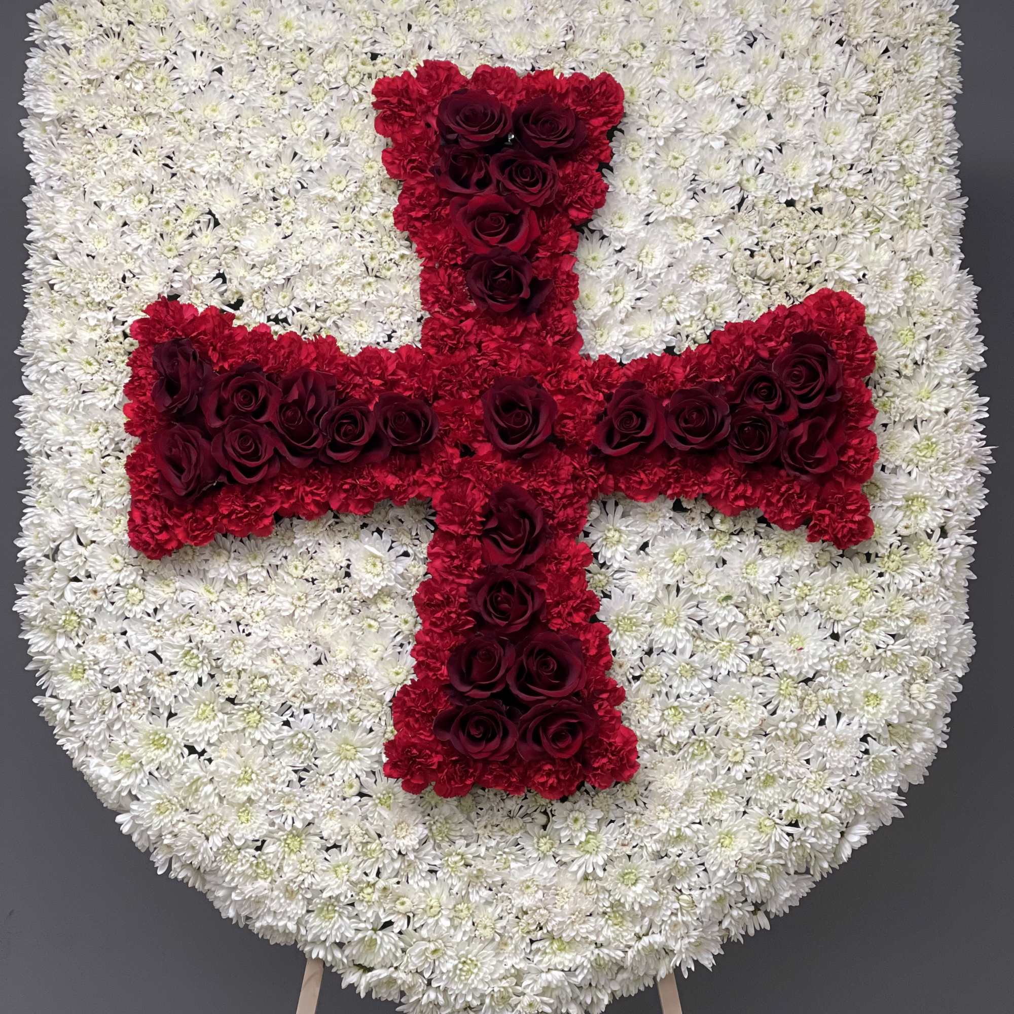 Heart-shaped floral tribute with a red cross on a white chrysanthemum base