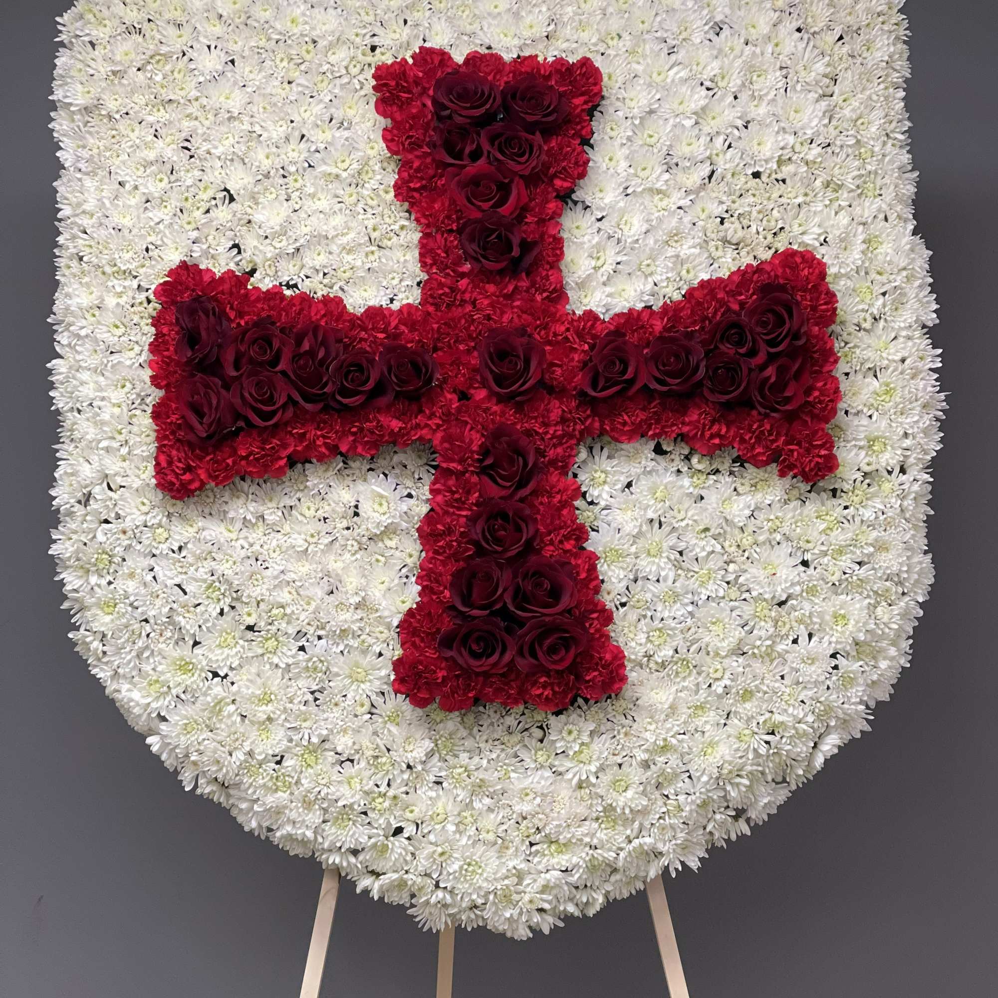 Heart-shaped floral tribute with a red cross on a white flower background