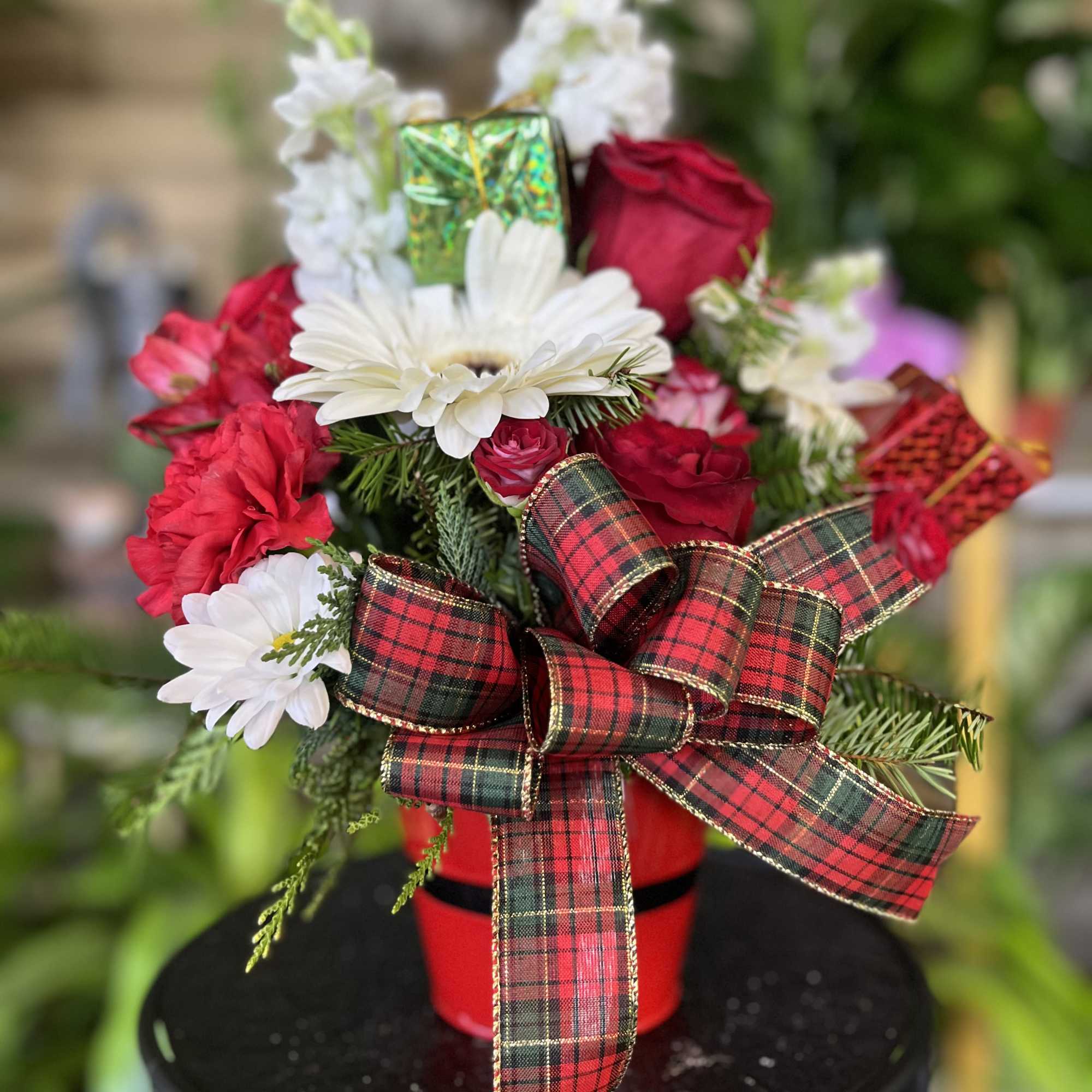 Red and white floral arrangement in a red container with a plaid bow