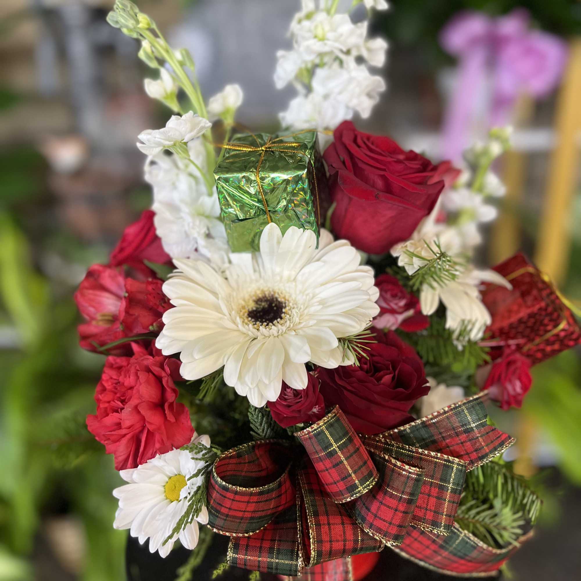Red roses and white daisies arranged with plaid ribbon and a small gift box.