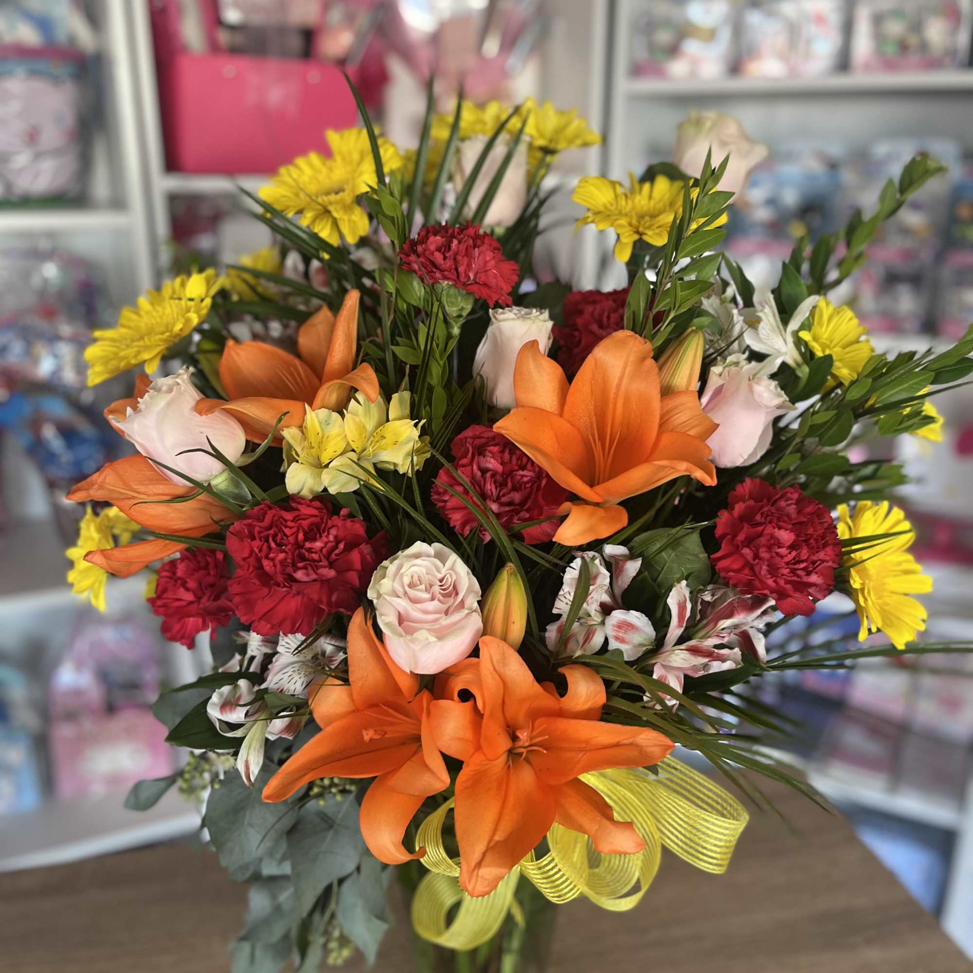 Mixed bouquet of orange lilies, pink roses, red carnations, and yellow daisies in a glass vase