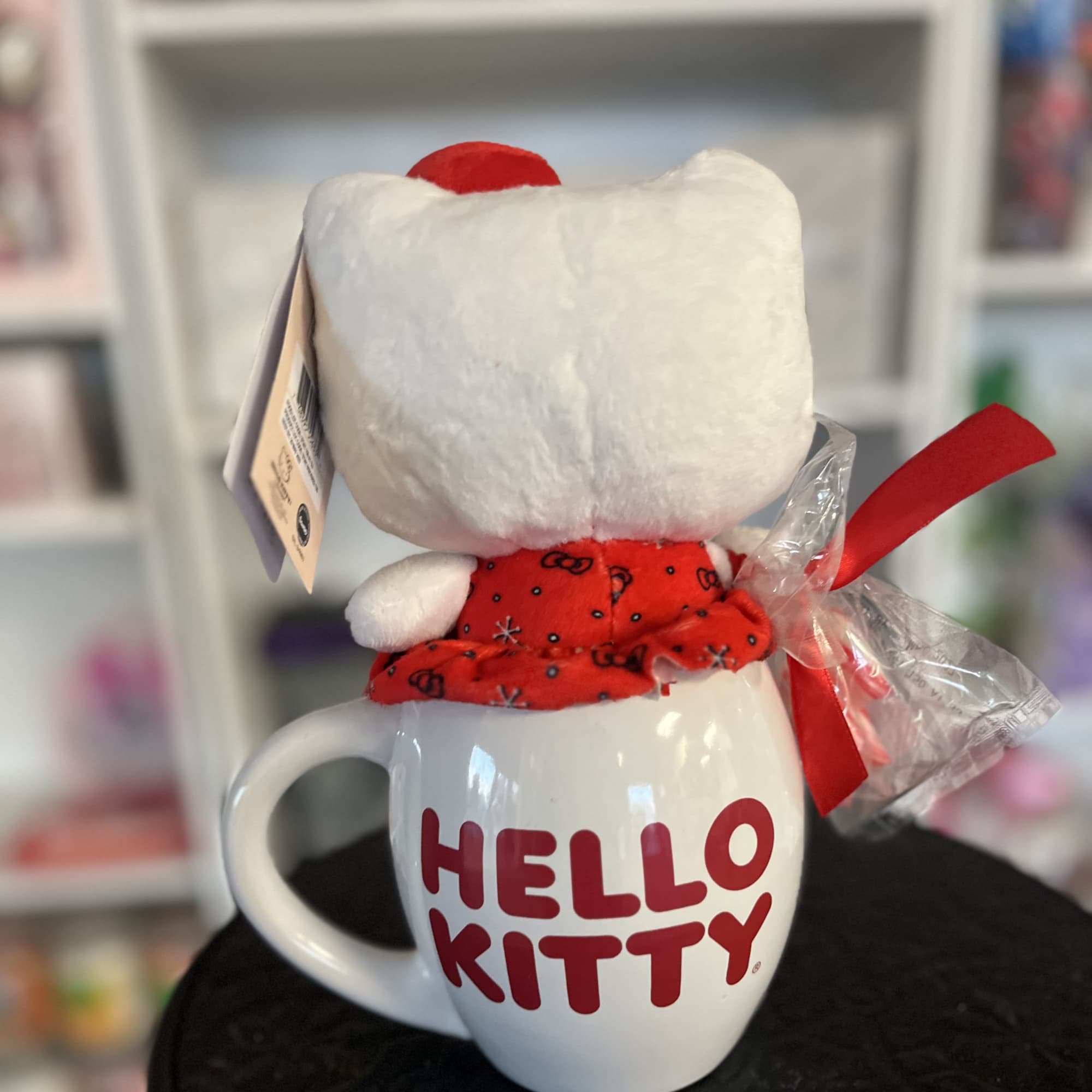 Hello Kitty plush sitting in a white mug with a red ribbon