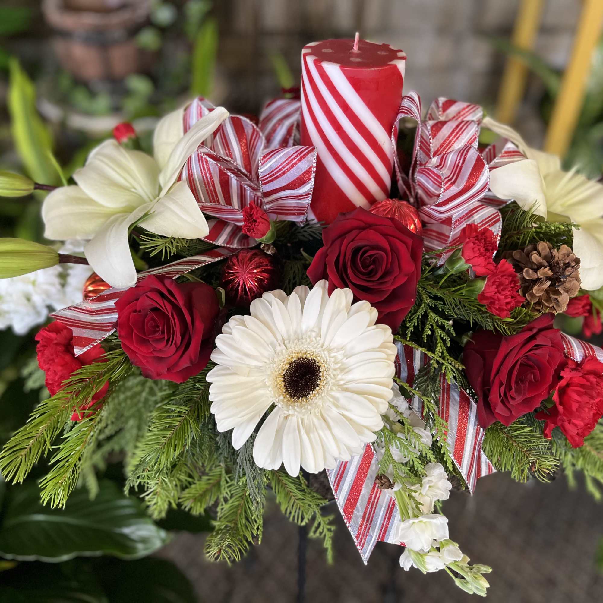 Red roses and white lilies arranged with a candle and striped ribbon