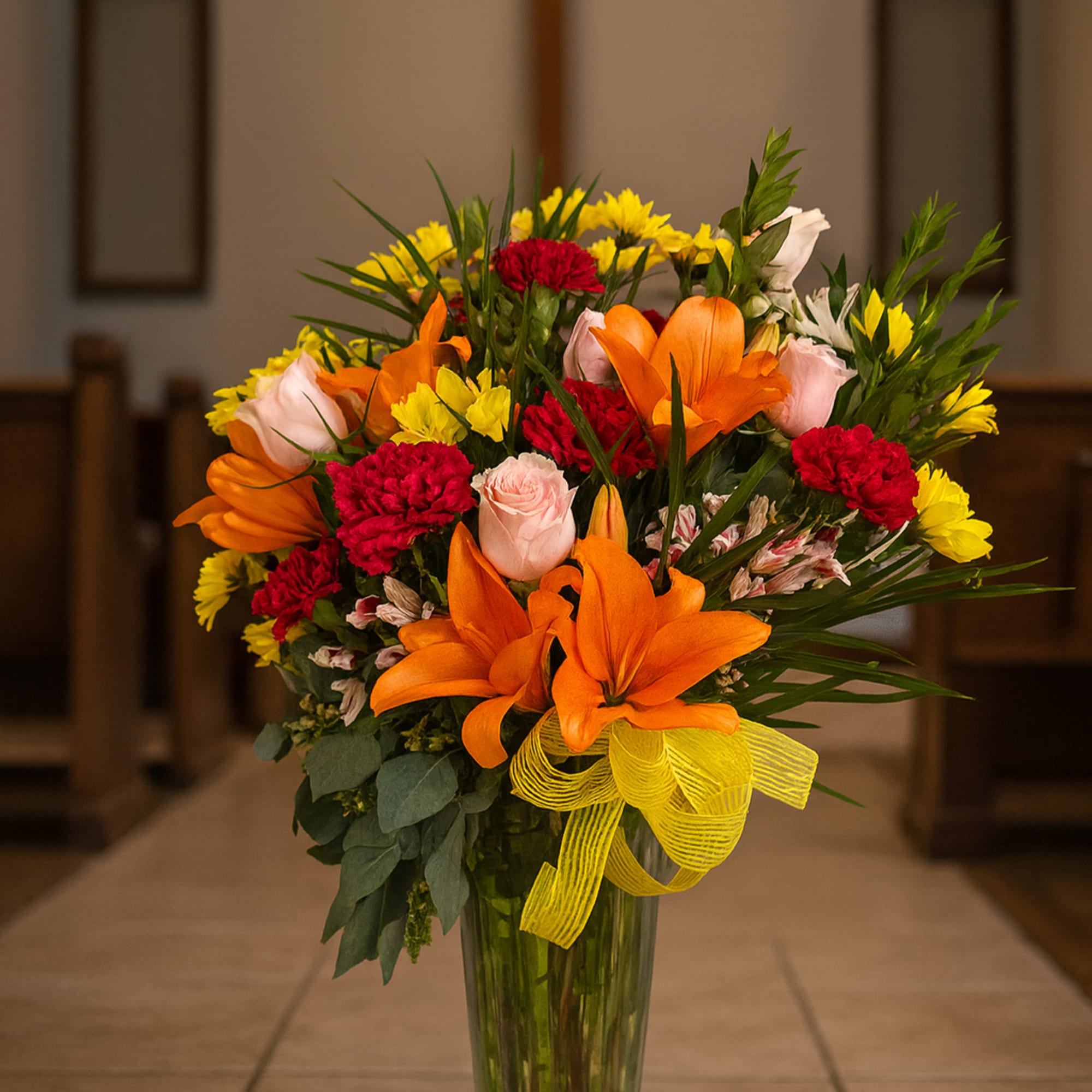 Colorful flower arrangement in a tall glass vase with a yellow ribbon