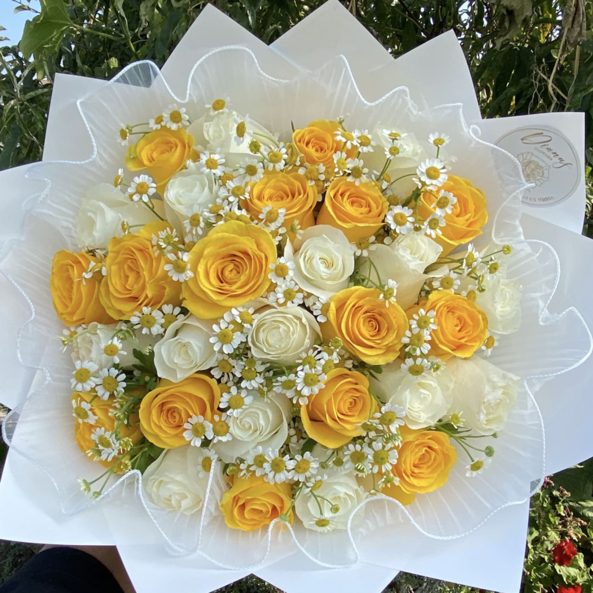 Bouquet of yellow and white roses with small daisy flowers wrapped in white paper