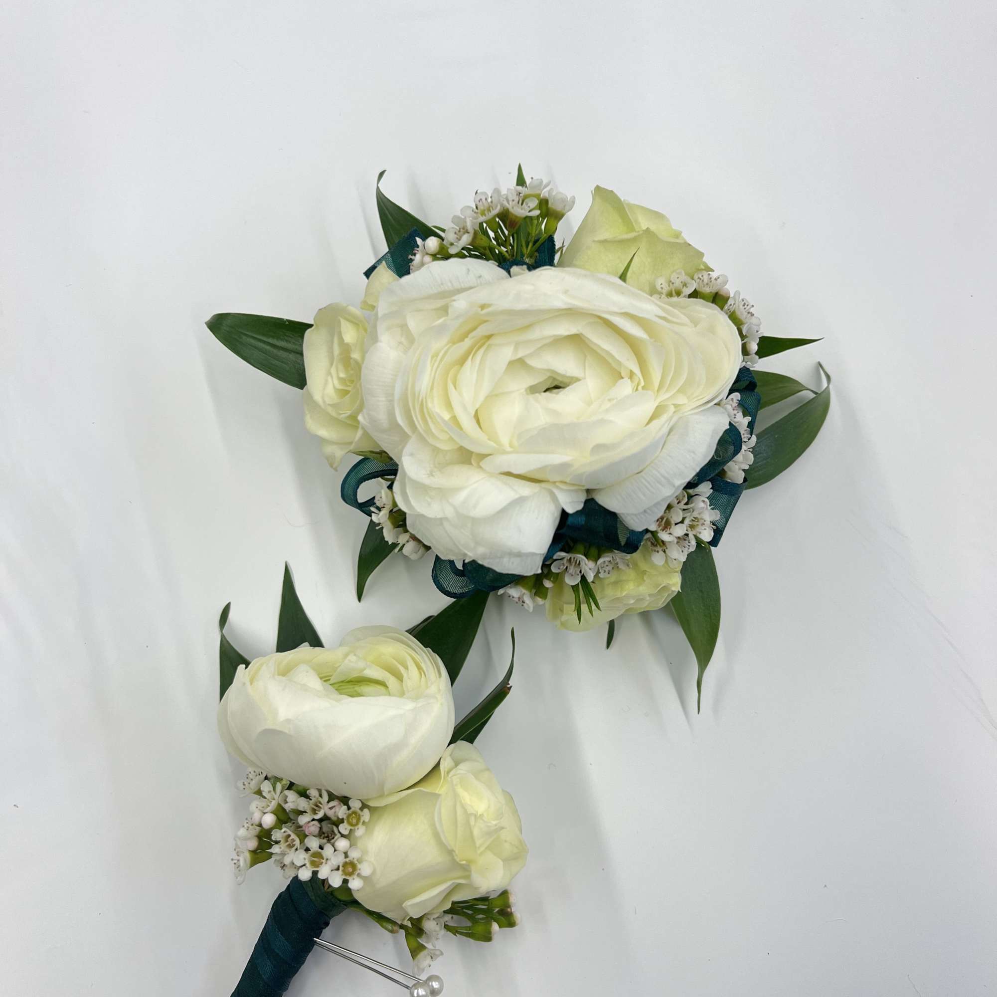 A white boutonniere and corsage set featuring elegant white roses and ranunculus