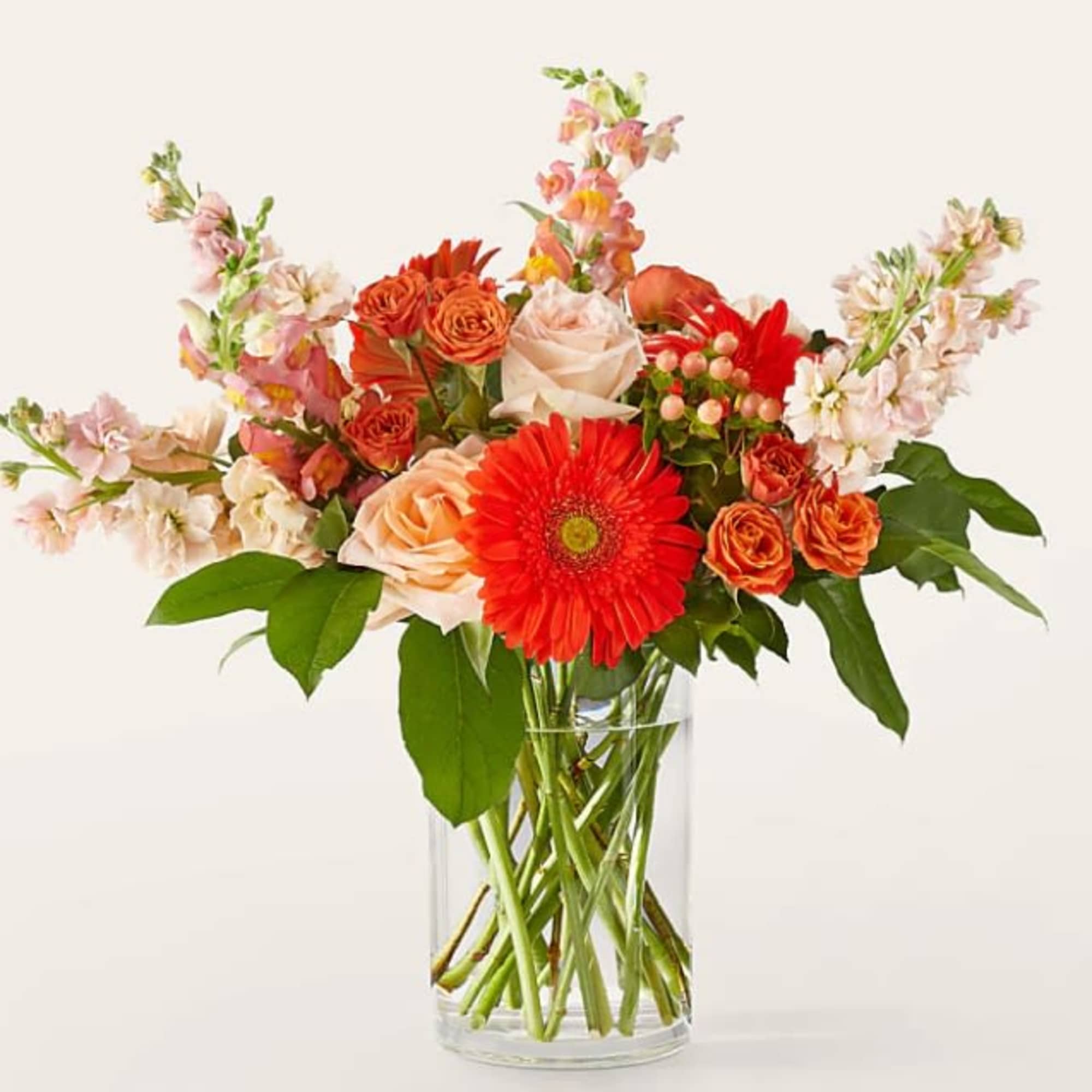 Mixed bouquet of orange, pink, and red flowers in a clear glass vase