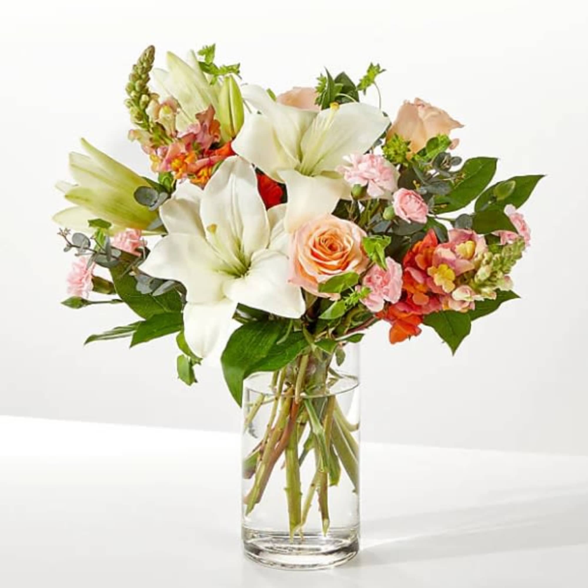 Bouquet of white lilies and peach roses in a clear glass vase