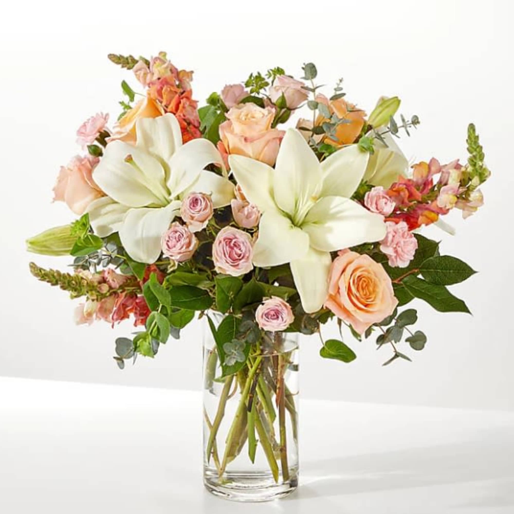 Bouquet of white lilies and peach roses in a clear glass vase