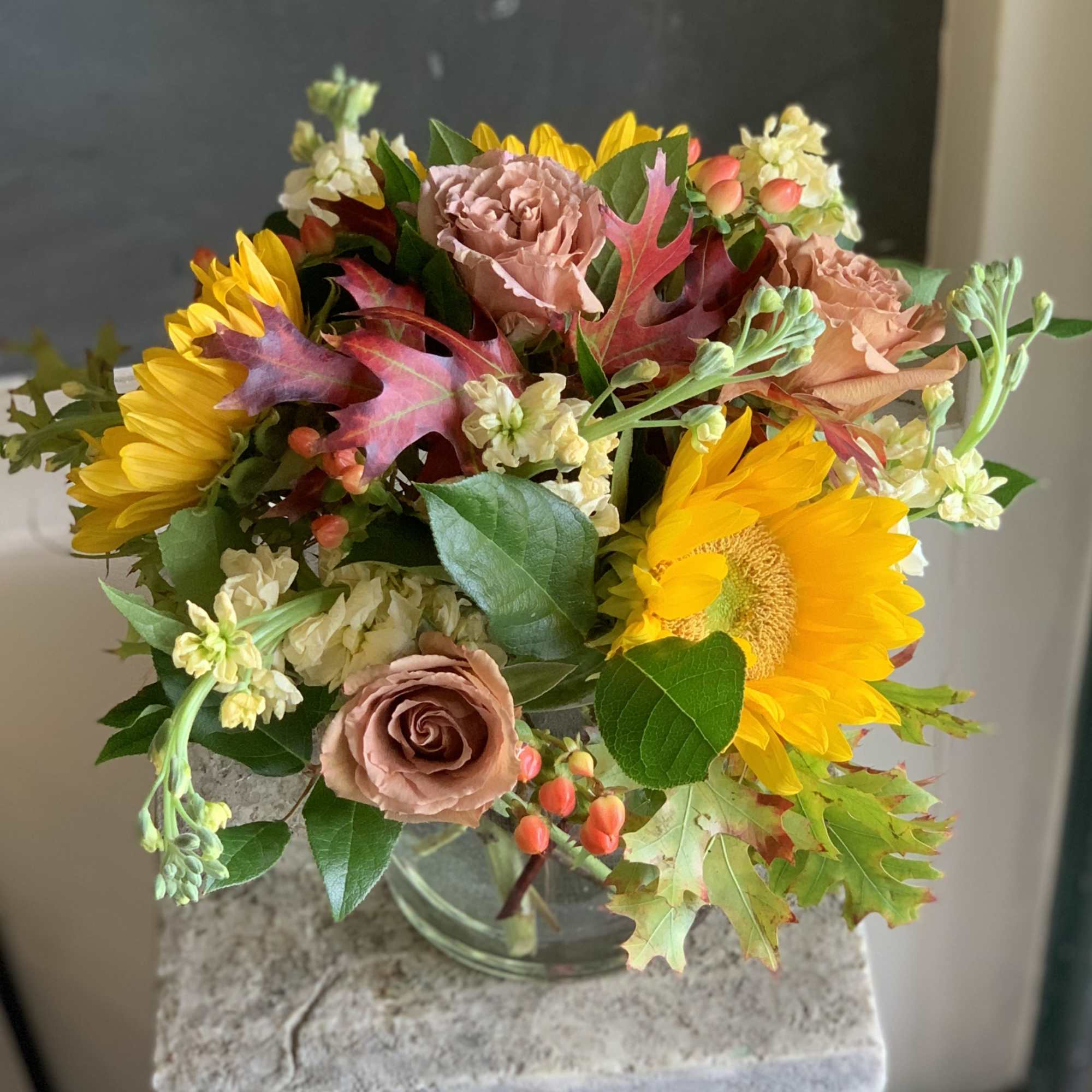 Bouquet of sunflowers, roses, and cream filler flowers in a glass vase