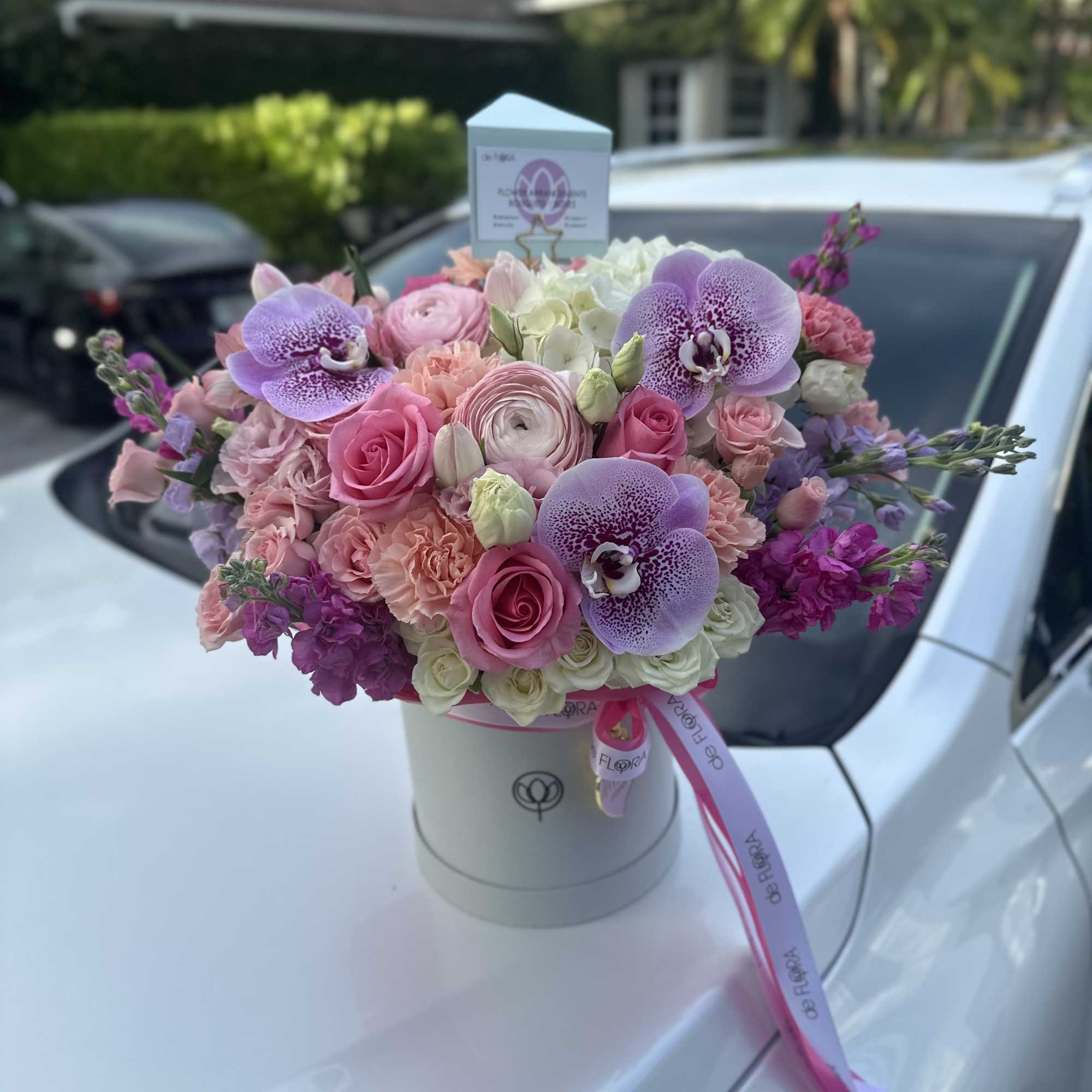 Round hatbox arrangement of pink roses, orchids, and mixed pastel flowers with ribbons
