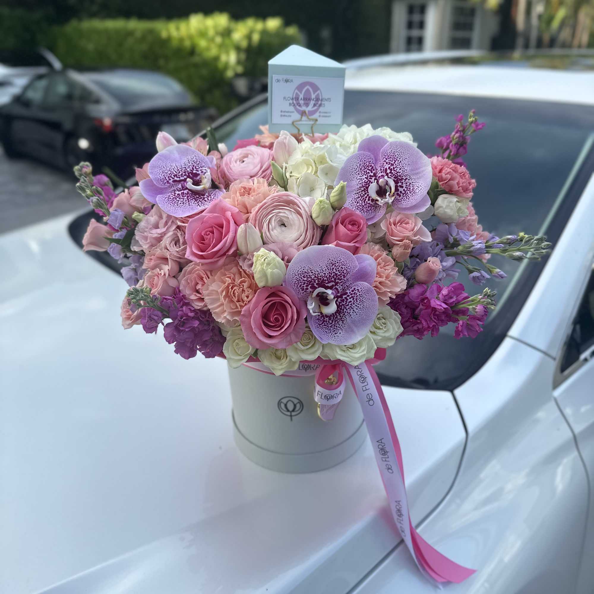 Round hatbox arrangement of pink and white roses with lavender orchids and mixed pastel blooms.