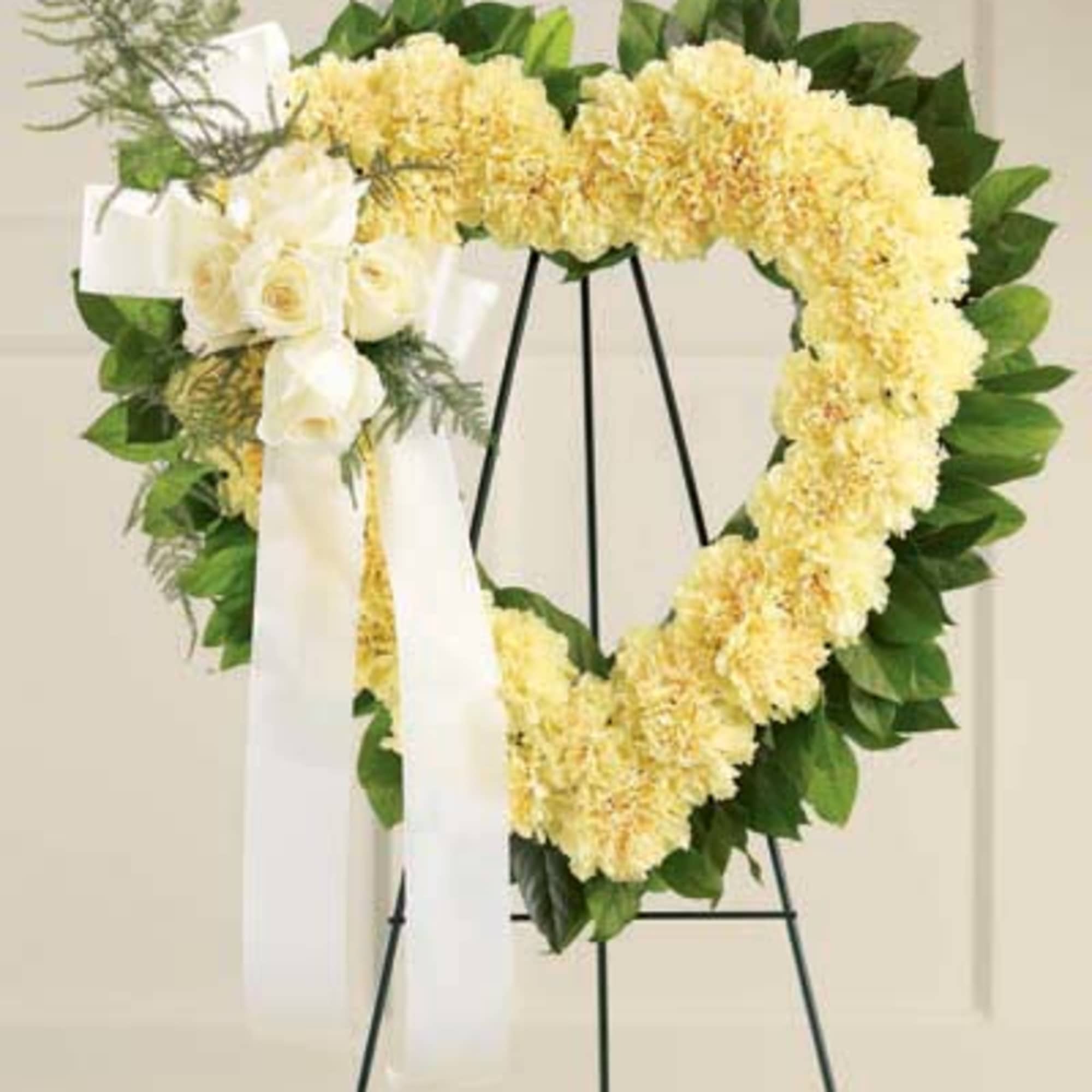 Heart-shaped yellow floral wreath on a black stand with white ribbon
