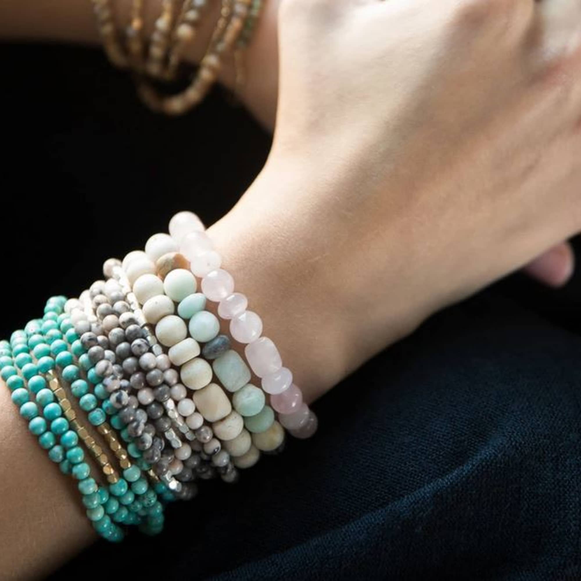 A wrist covered with stacked beaded bracelets in pastel colors.