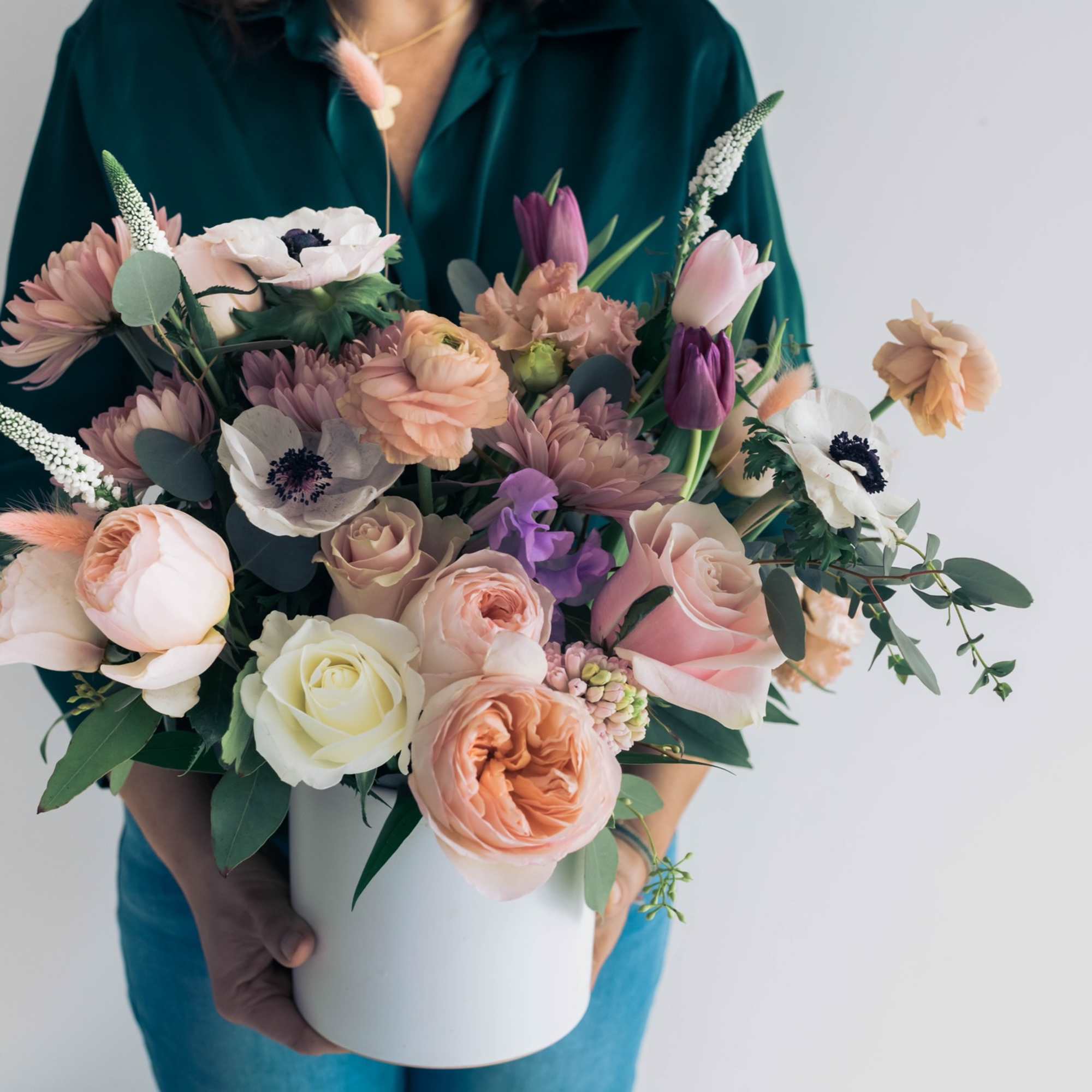 Mixed pastel bouquet in a white vase held by a person
